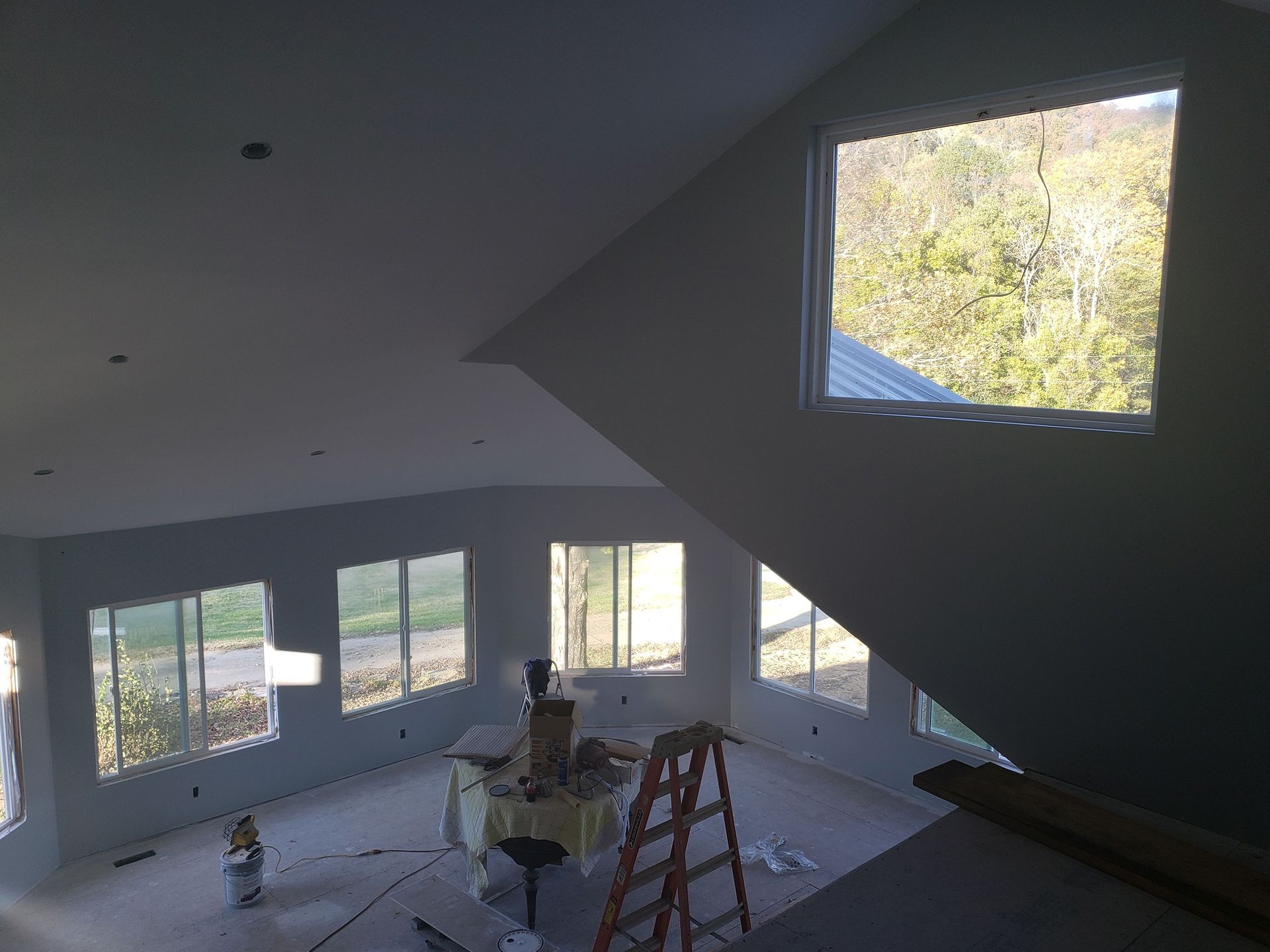 Interior view of a room with multiple windows and a ladder; construction in progress.