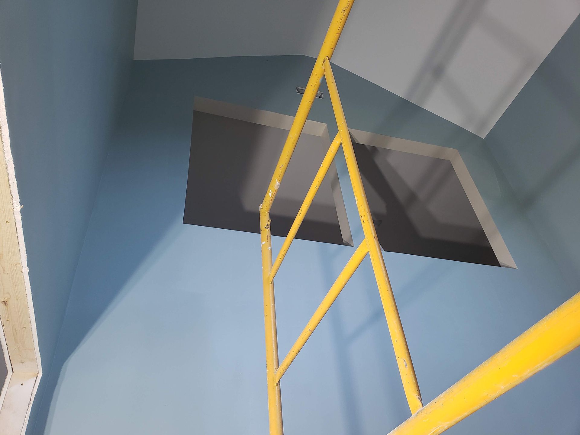 Interior of a room with blue walls, a yellow scaffold, and a window.
