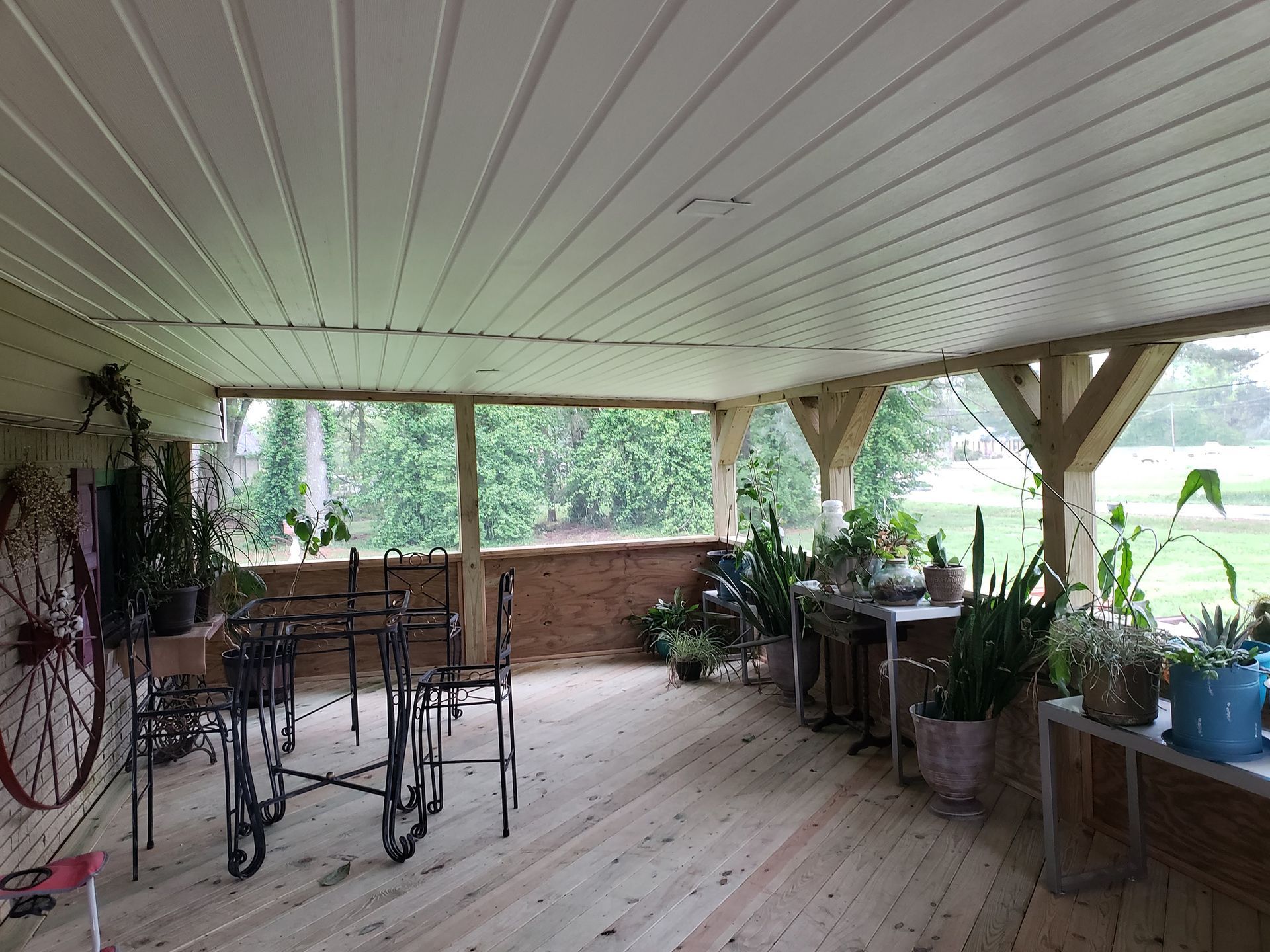 Covered porch with plants, metal furniture, and a wooden deck.