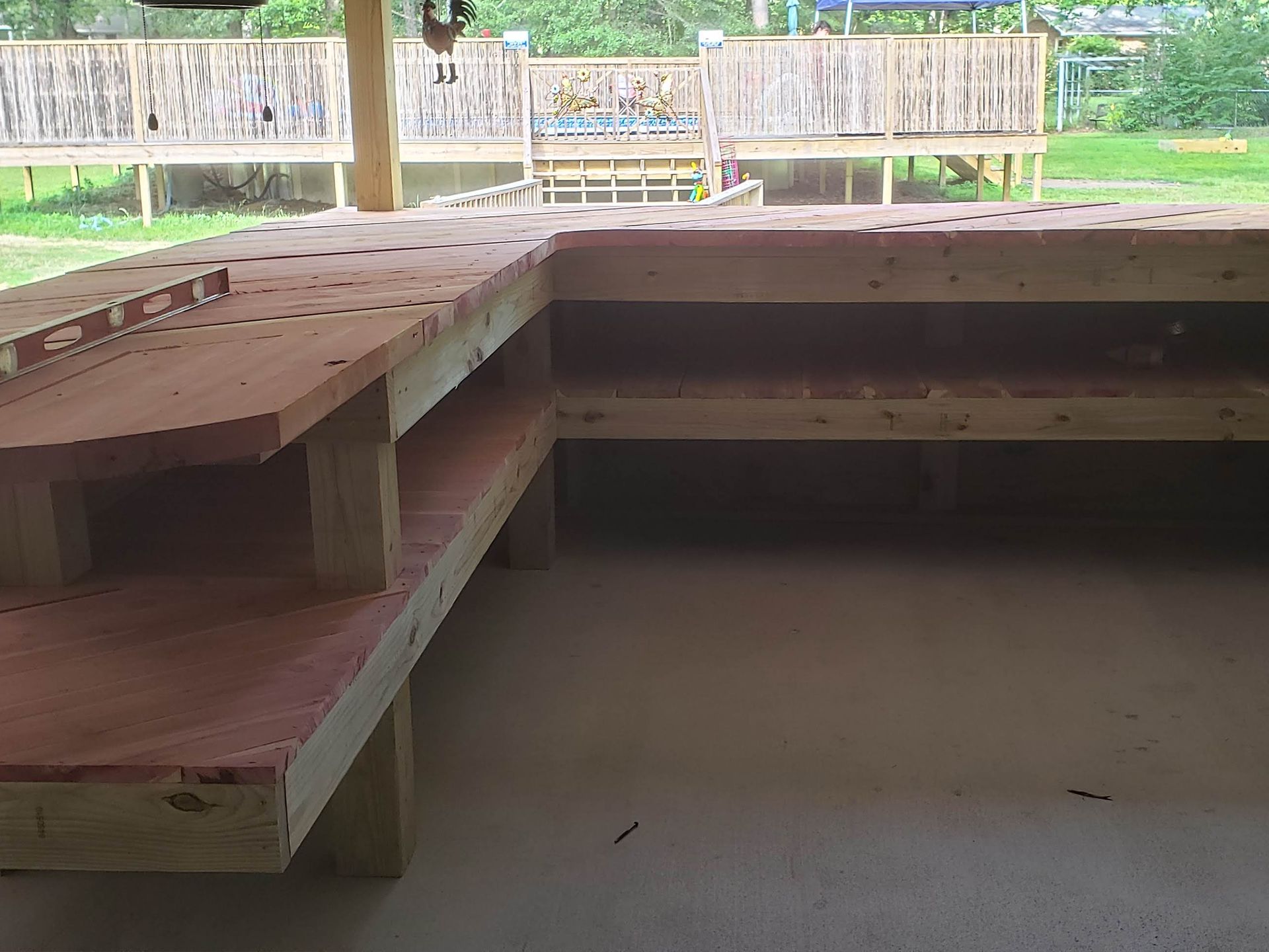 L-shaped wooden outdoor bar with shelves and drilled holes, likely for tools or glasses, on a concrete patio.