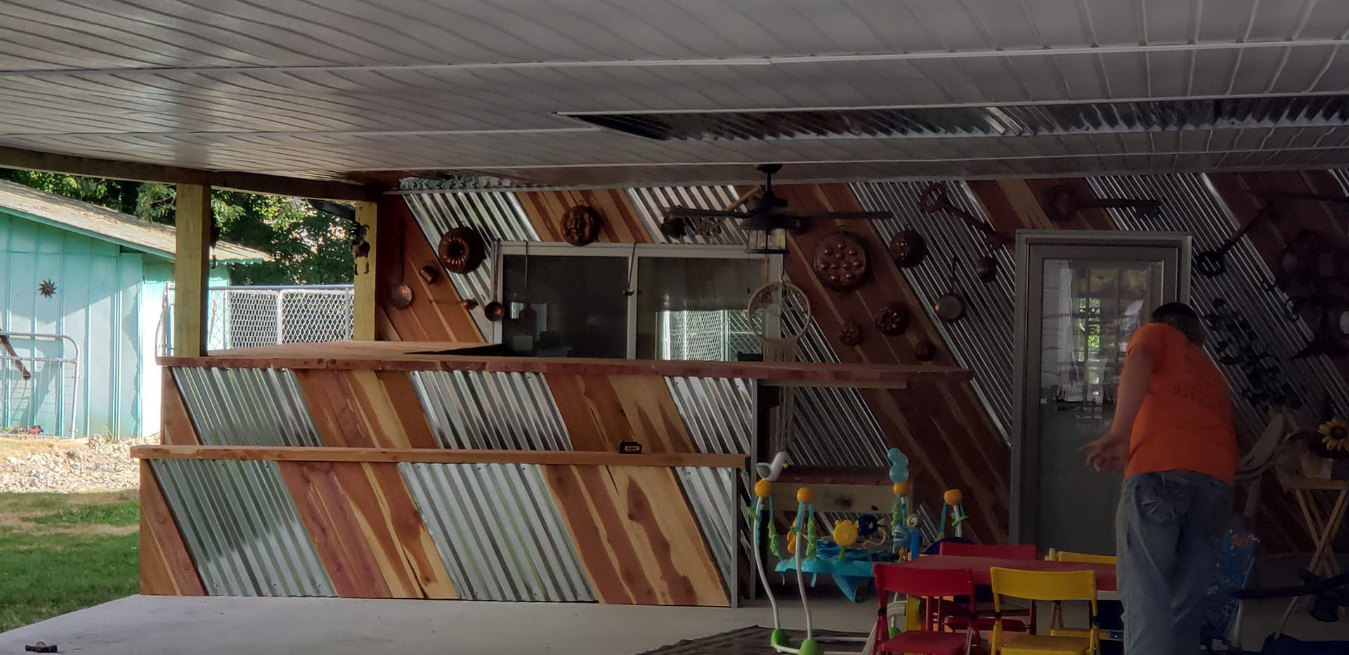 Outdoor bar with corrugated metal and wood accents, a person stands near the door.