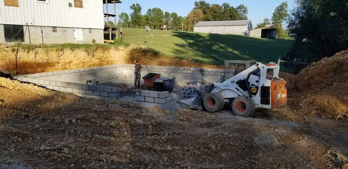 A white Bobcat working on a construction site, near a building and a green hill.