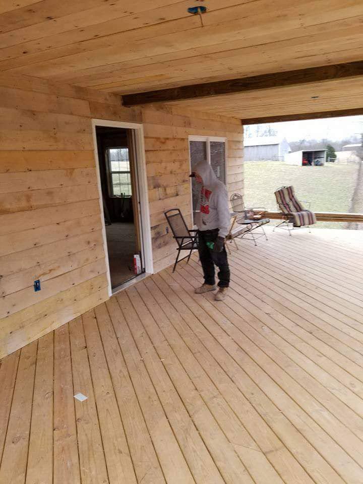 Person on unfinished wooden deck, with door and window visible; exterior setting with grass.