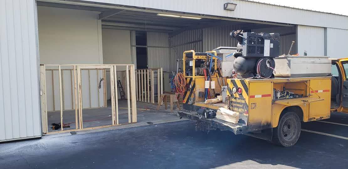 Yellow work truck parked in front of an open warehouse with wood frames.