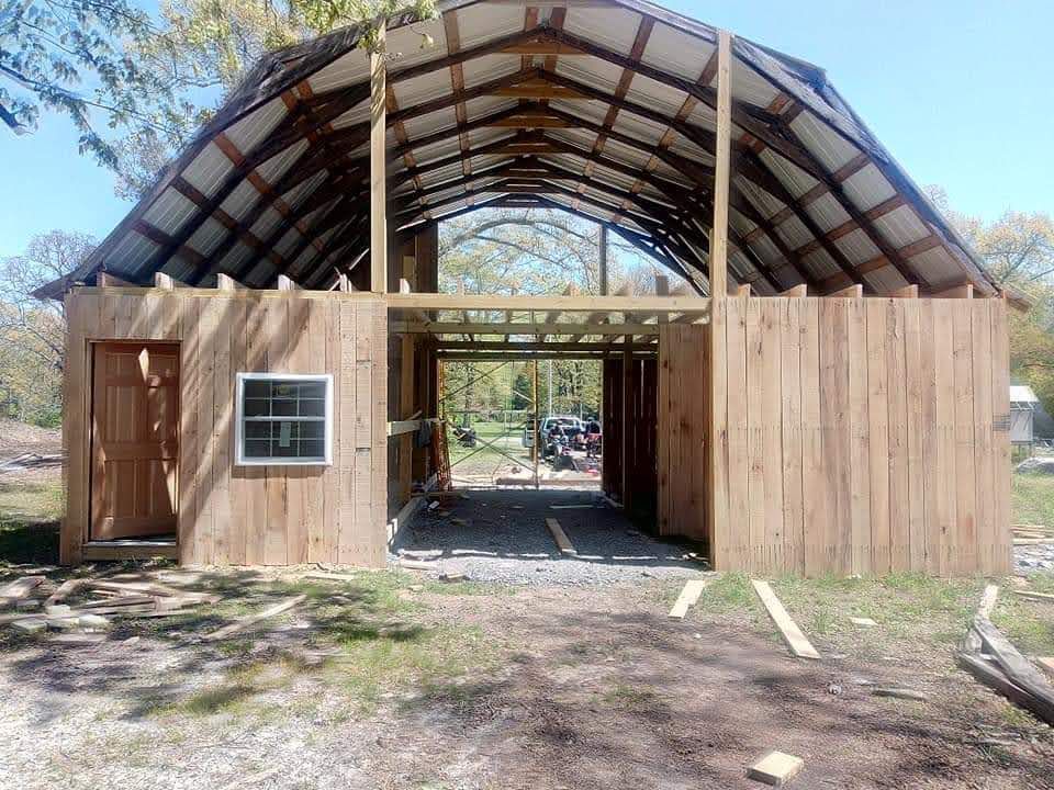 Barn under construction; wood siding, open doorway, unfinished roof, natural setting.