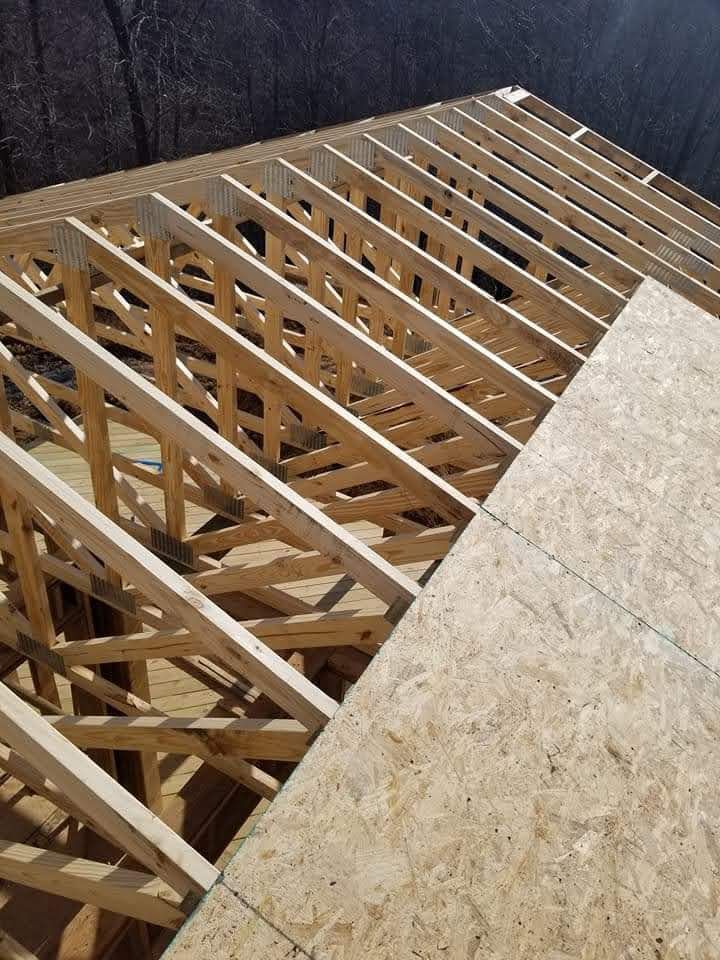 Wooden roof trusses and sheathing on a construction site, sunny day.