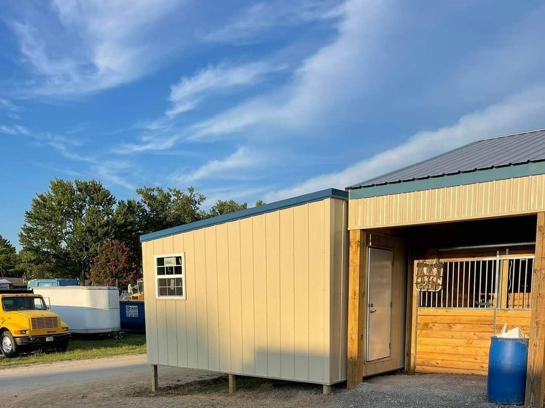 Small shed and stable under blue sky, yellow truck nearby.