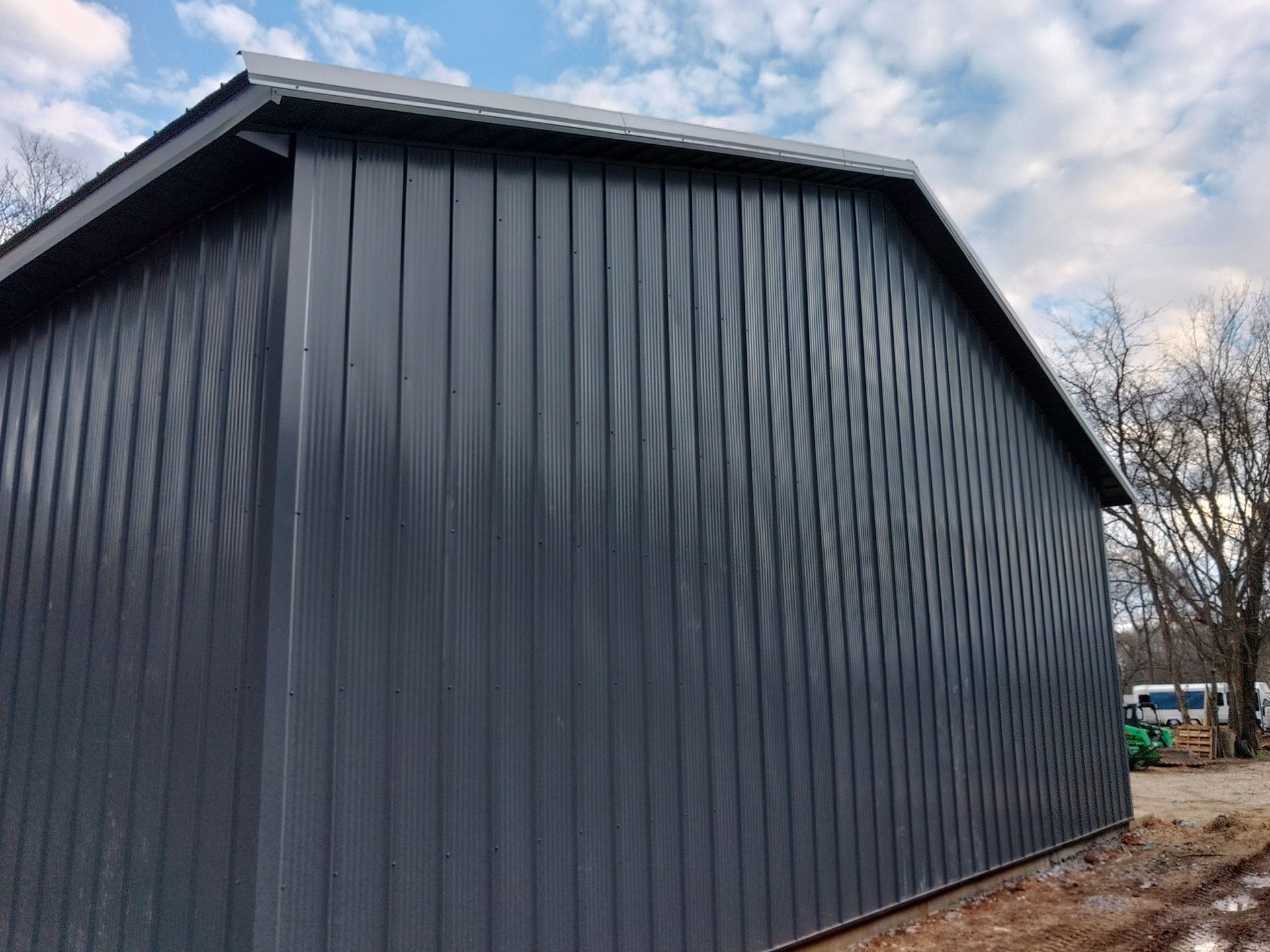Dark grey metal barn with vertical siding under a cloudy sky.
