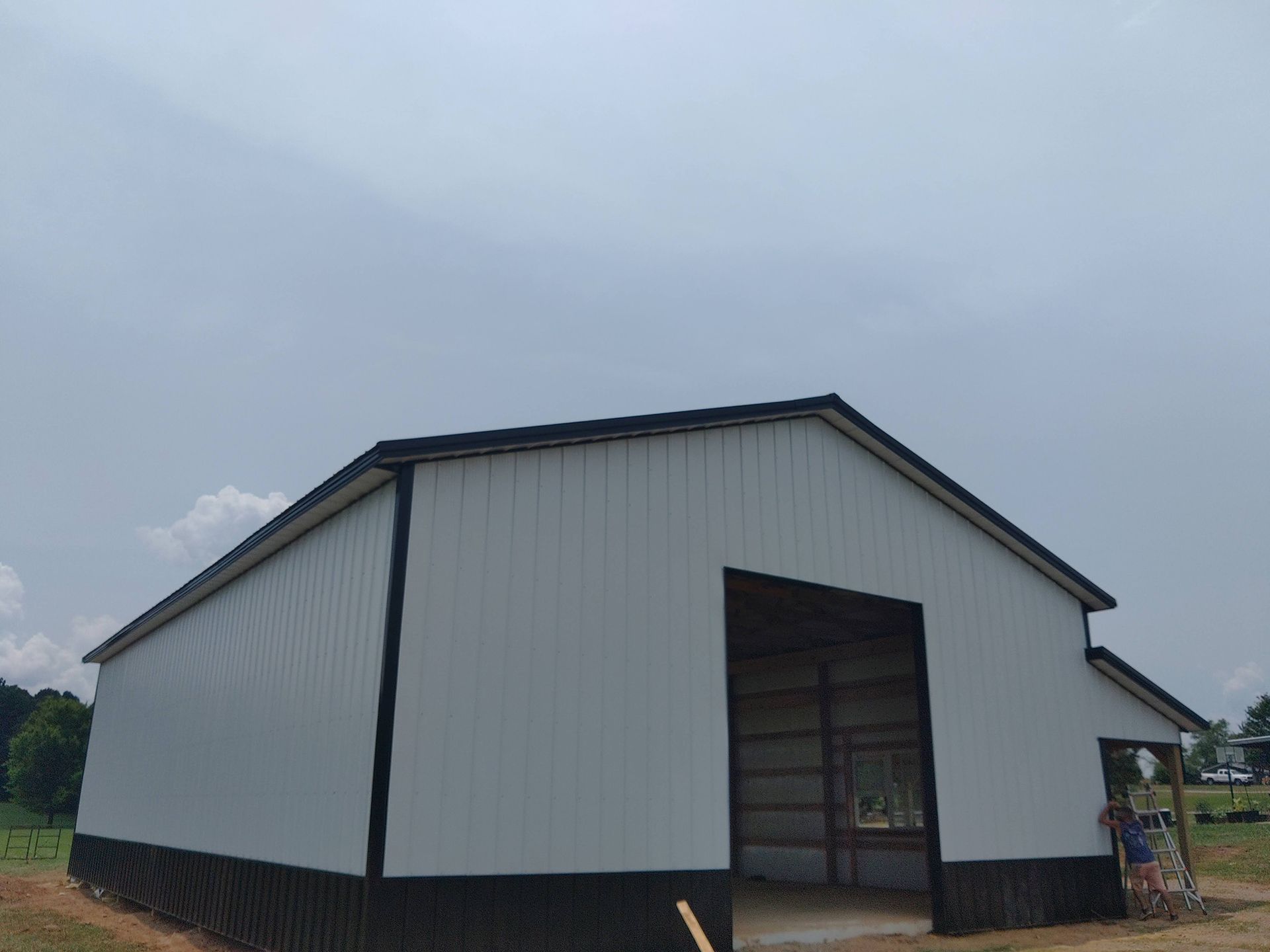 White and black metal barn with open door under cloudy sky.
