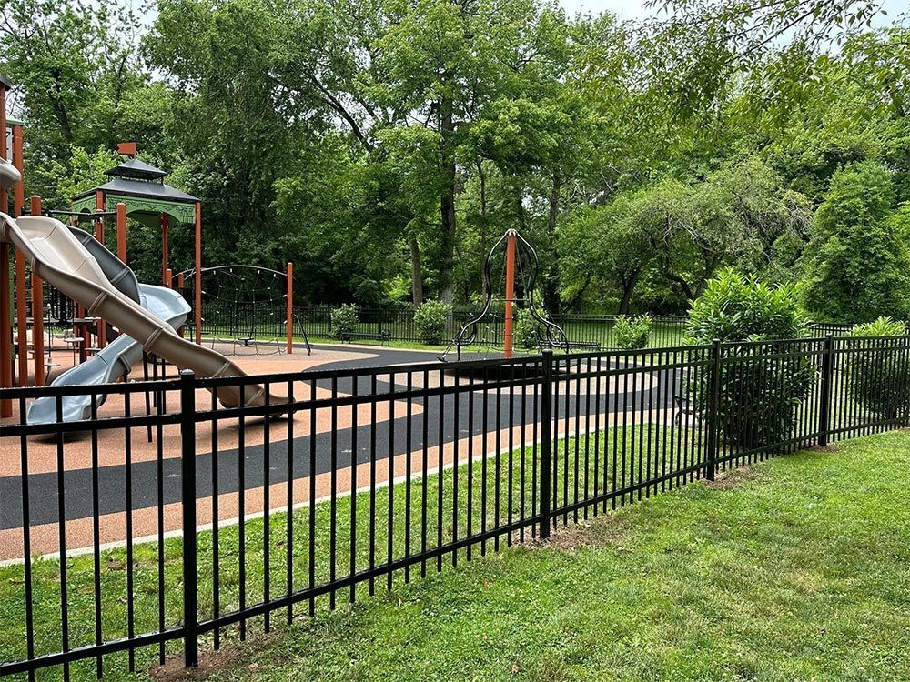 Black metal fence surrounds a children's playground with a slide. Trees are in the background.