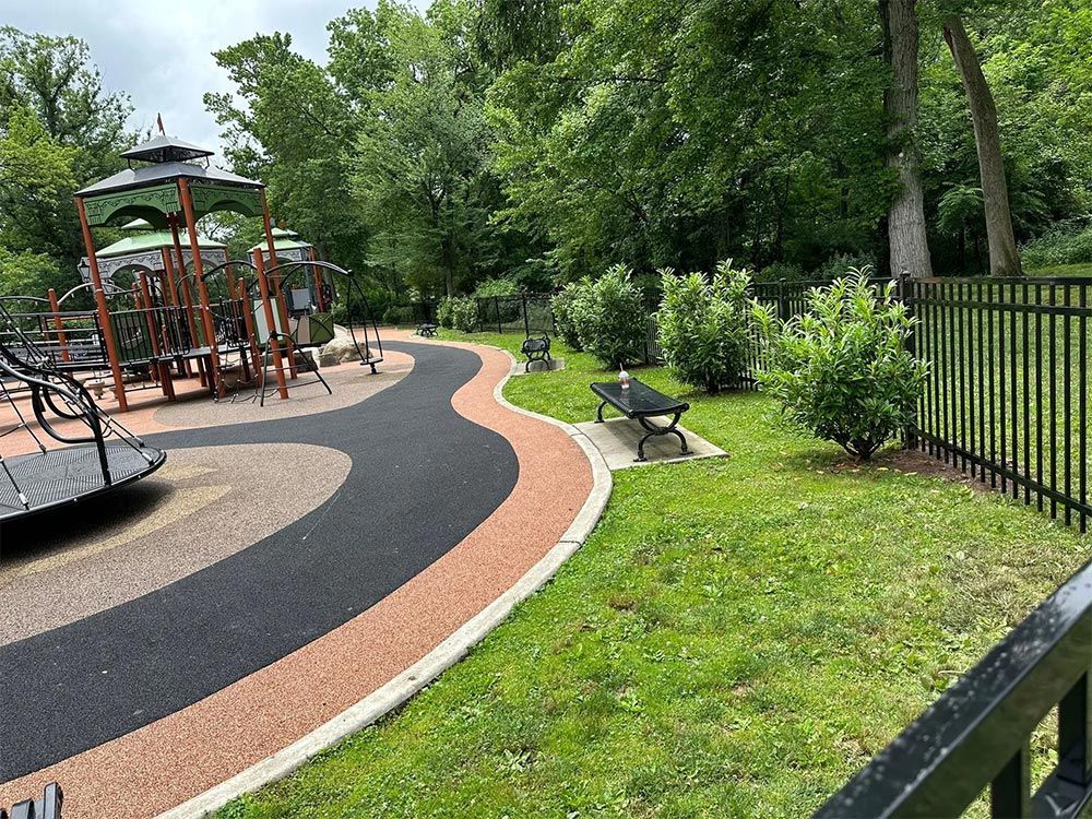 Playground with a black fence, winding path, trees, and play structures.