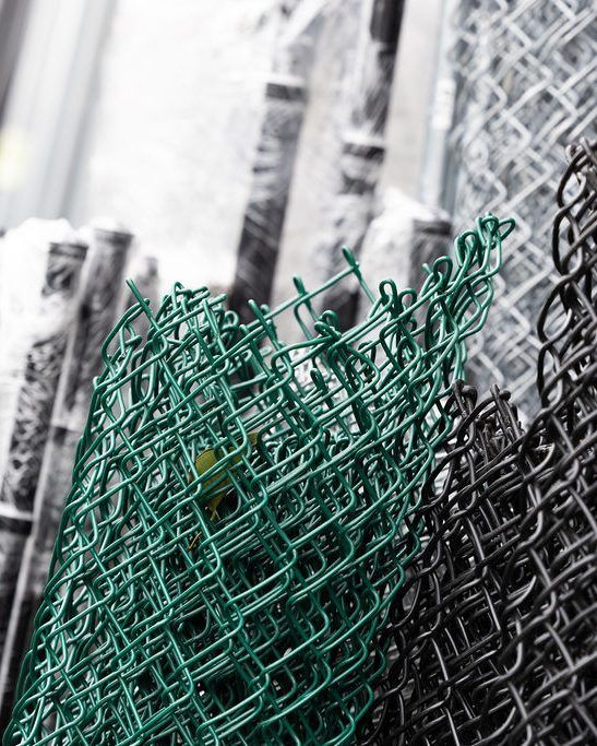 Green and black chain link fencing rolls, stacked.