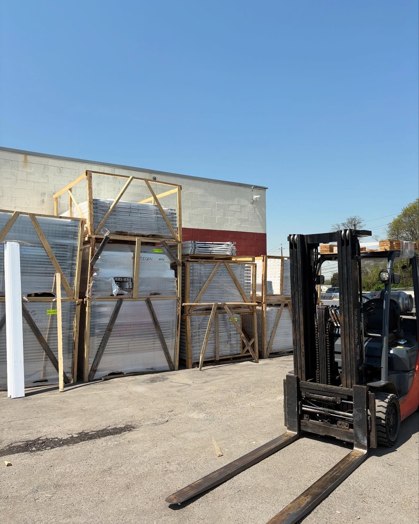 Forklift near a building with wooden frames holding materials on a sunny day.