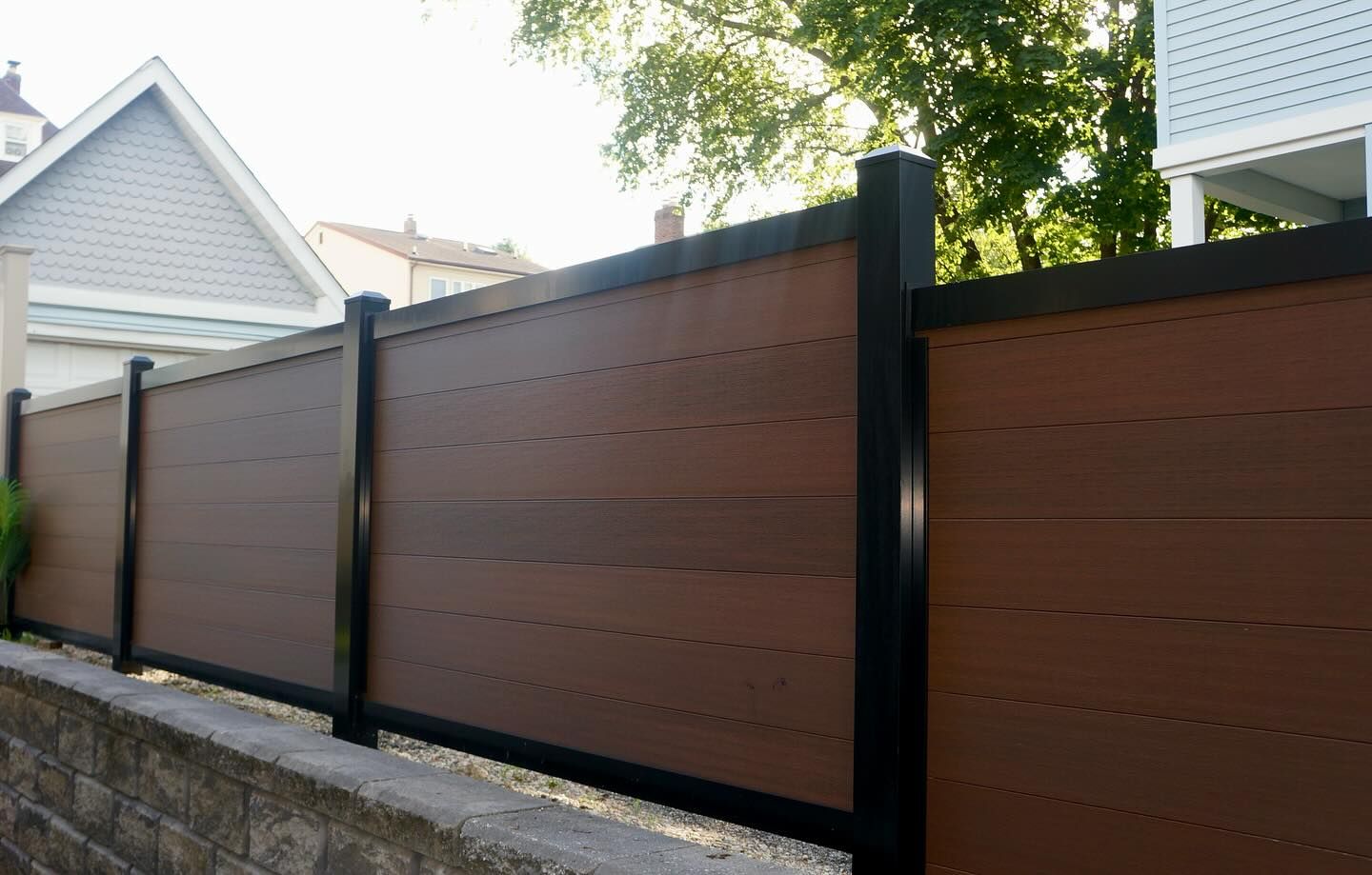 Brown horizontal plank fence with black posts, built on a low stone wall.