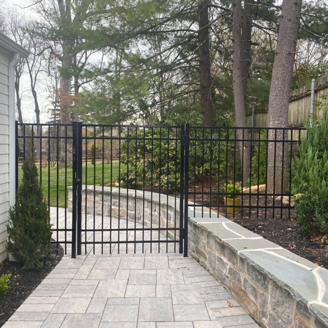 Black metal gate and fence on a stone path, leading to a backyard.