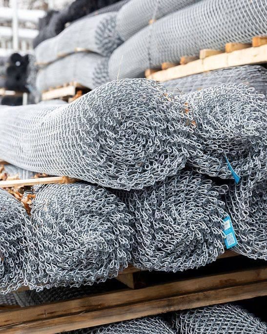 Rolls of silver metal mesh fencing stacked on a wooden pallet.