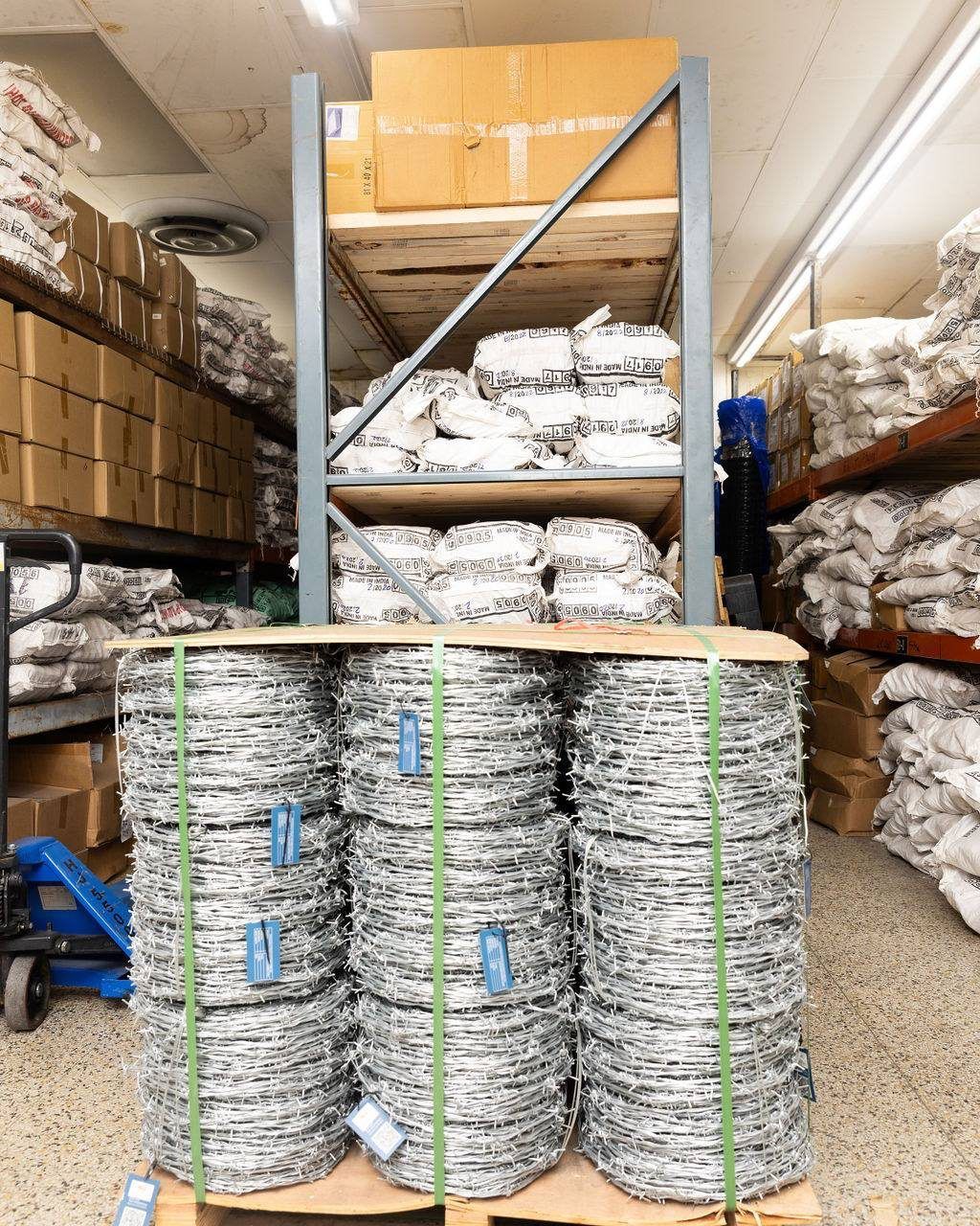 Pallet of barbed wire rolls in warehouse, under shelving with boxes.