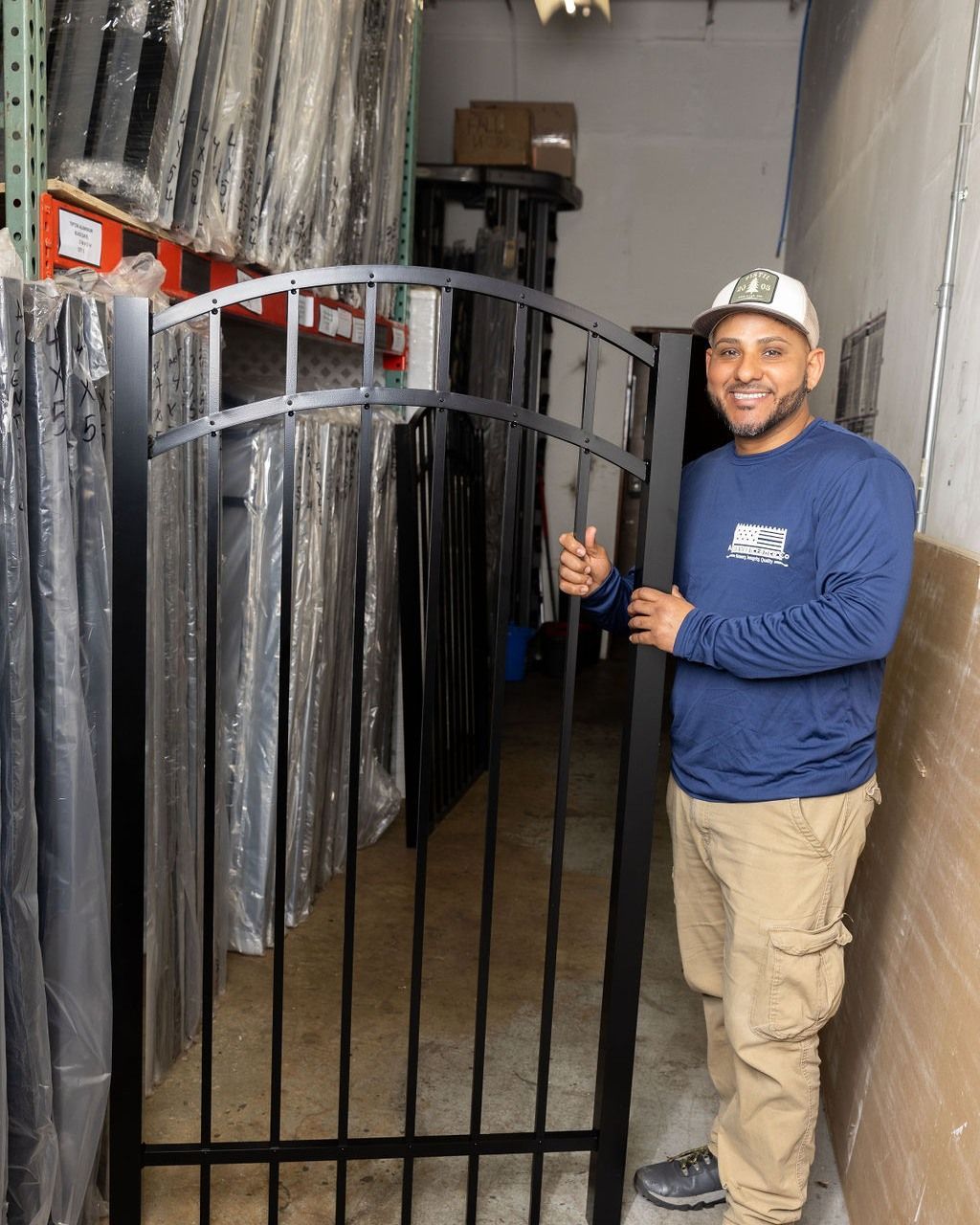 Man holds a black metal gate in a warehouse. He smiles, wearing a blue shirt and khaki pants.