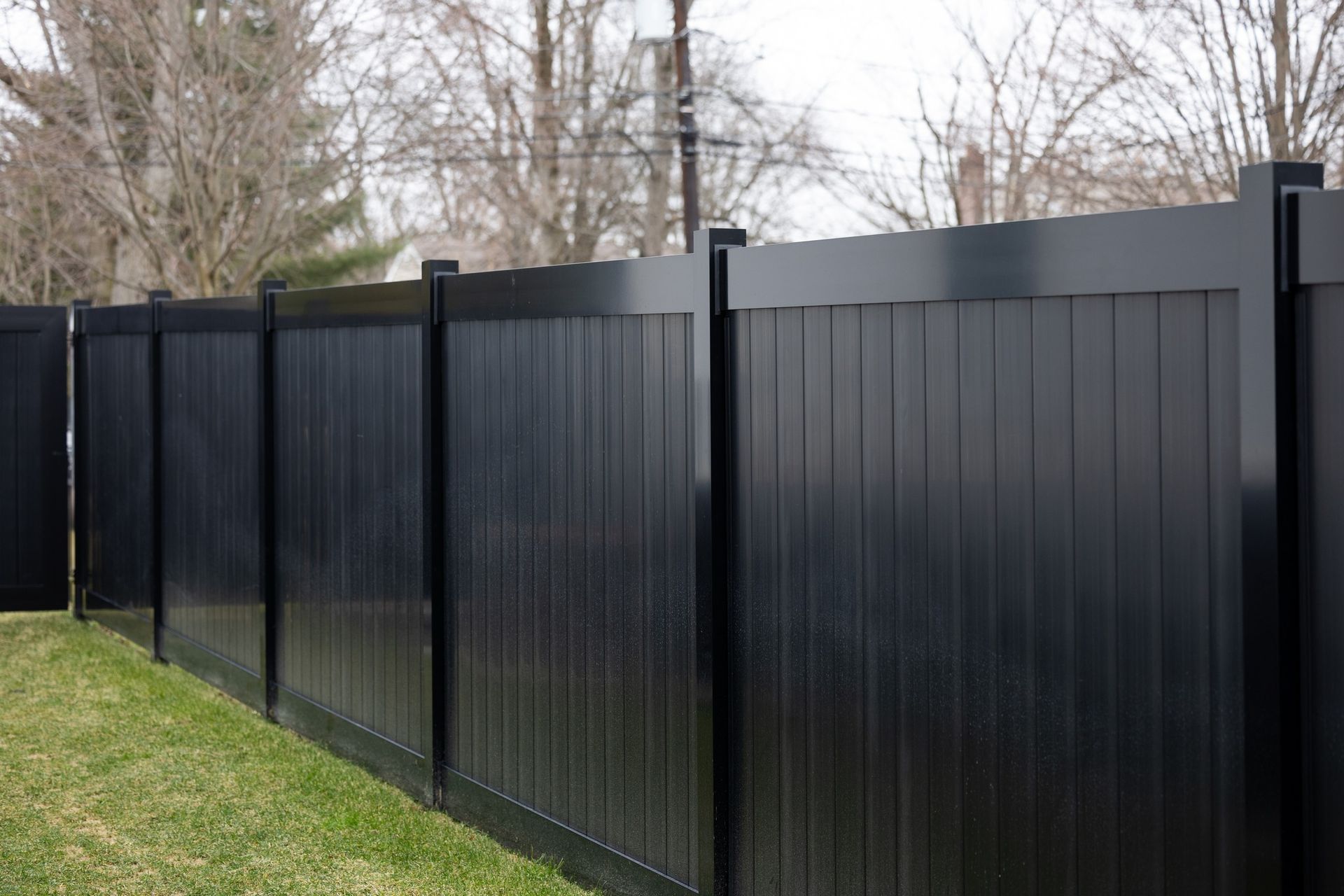 Black vinyl privacy fence in a residential yard with green grass.