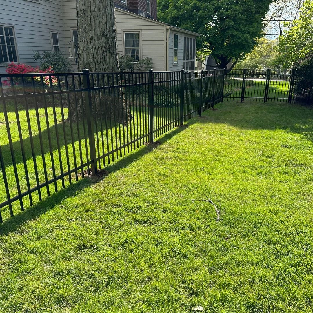 Black metal fence encloses a green grassy yard in front of a white house.