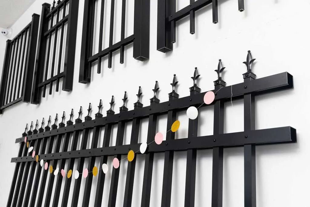 Black metal fence and gate with stone pillars, fronting a driveway. Trees in the background.