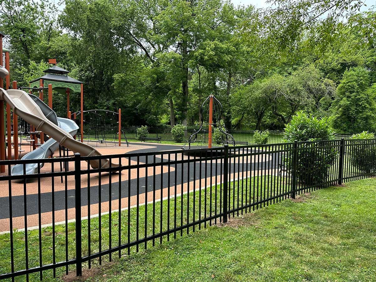 Black fence surrounds a playground with slides and trees in the background.
