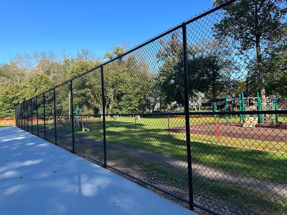 Black chain-link fence bordering a concrete path next to a grassy area with playground equipment.