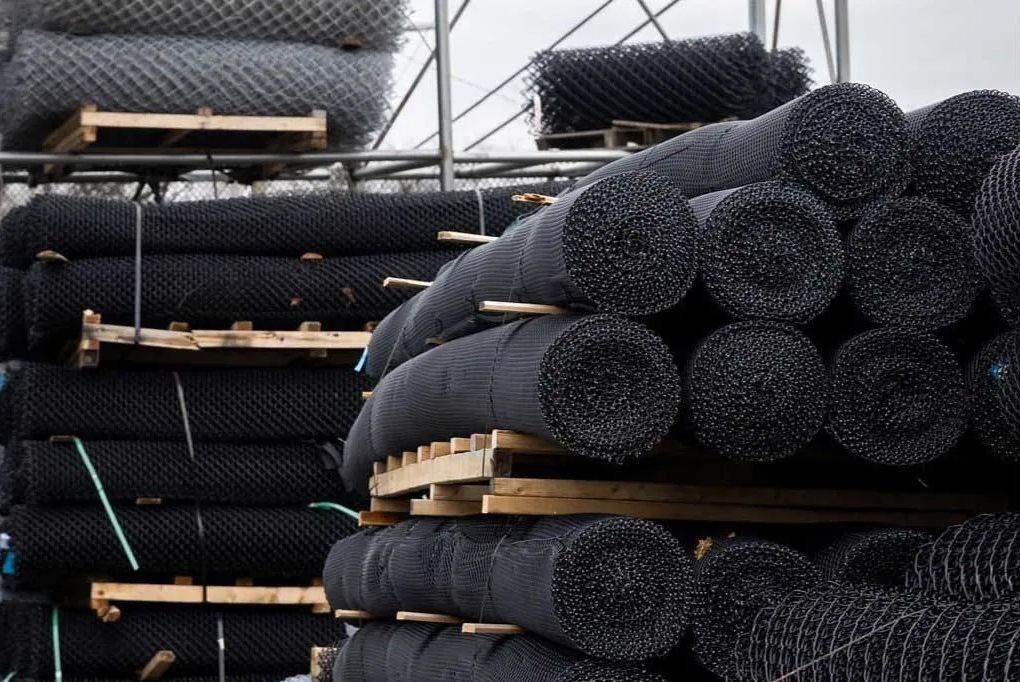Rolls of black fencing material stacked on wooden pallets.