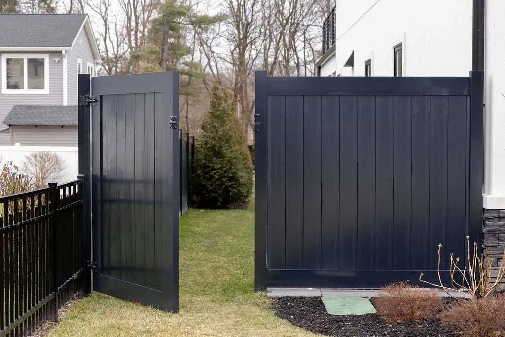 Black gate open onto a grassy yard with a house and black fence.