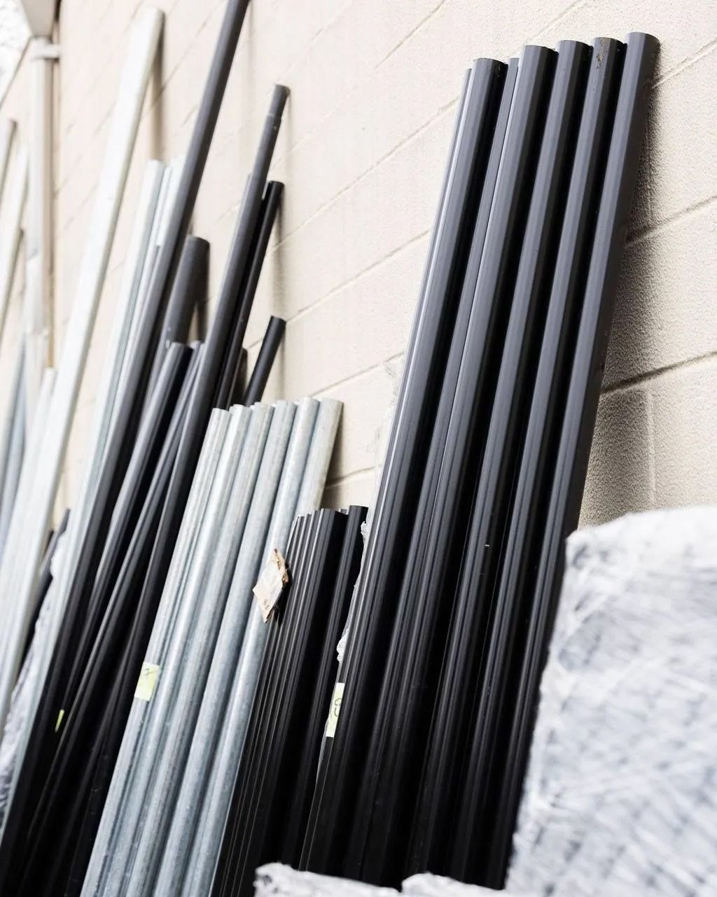 Black and gray metal poles leaning against a beige wall, possibly for construction.