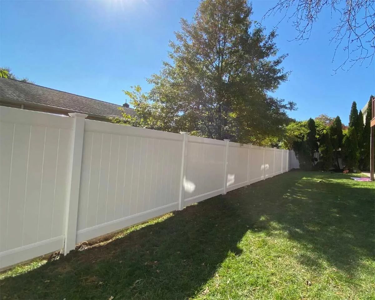 White vinyl fence in a sunny backyard with green grass and trees.