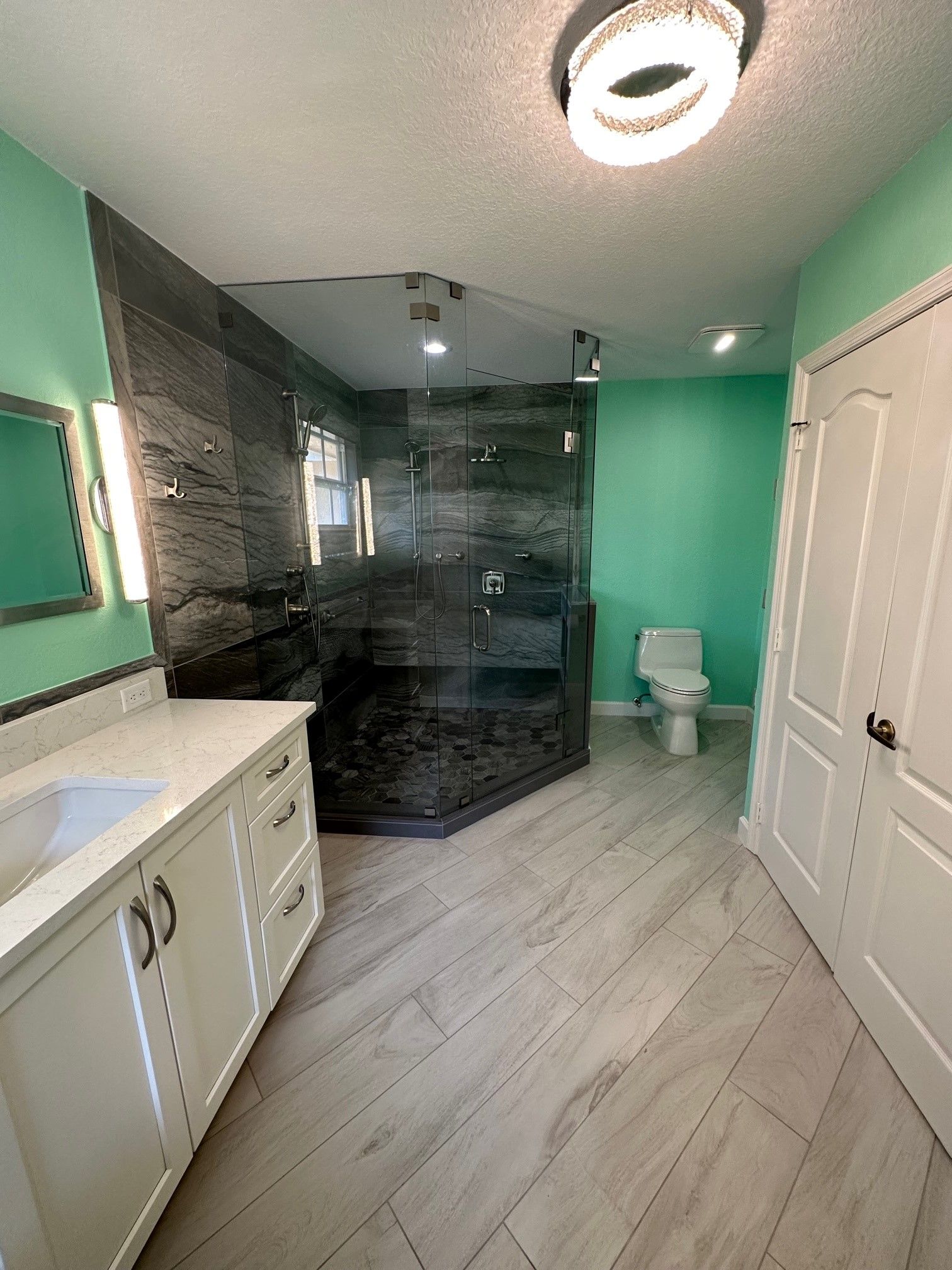 Bathroom with walk-in shower, vanity, toilet, and mint green walls. Light wood-look flooring. Recessed ceiling light.