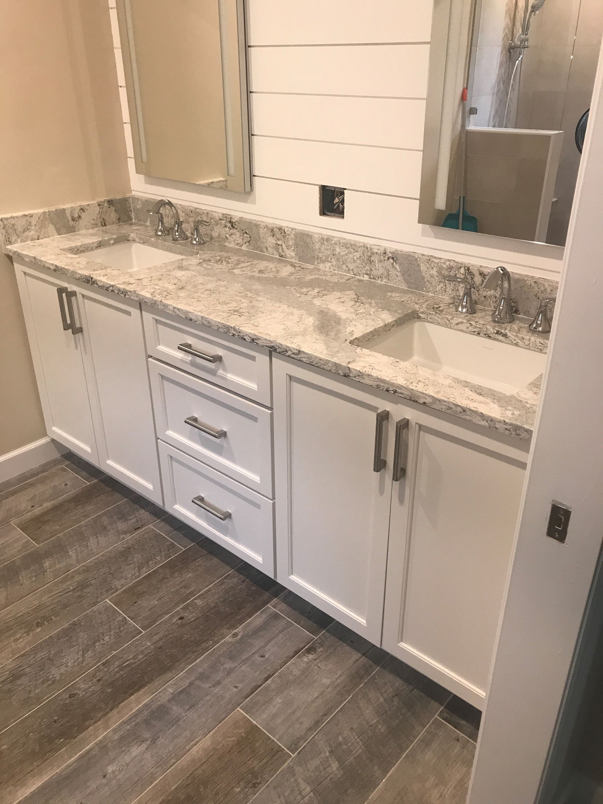 White bathroom vanity with granite countertop, white cabinets, and wood-look tile flooring.