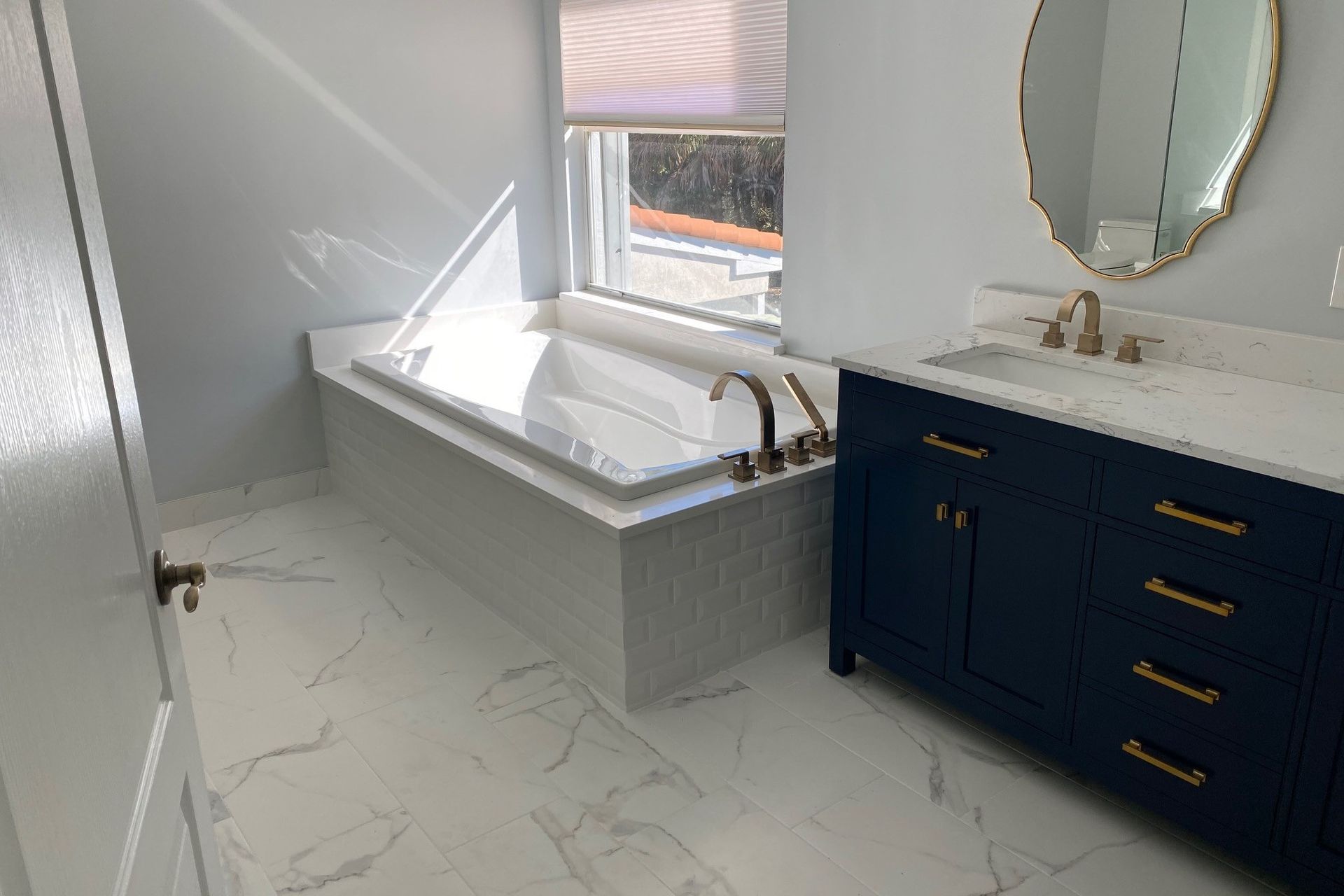 Bathroom with white tub, blue vanity, marble floor, and gold fixtures.