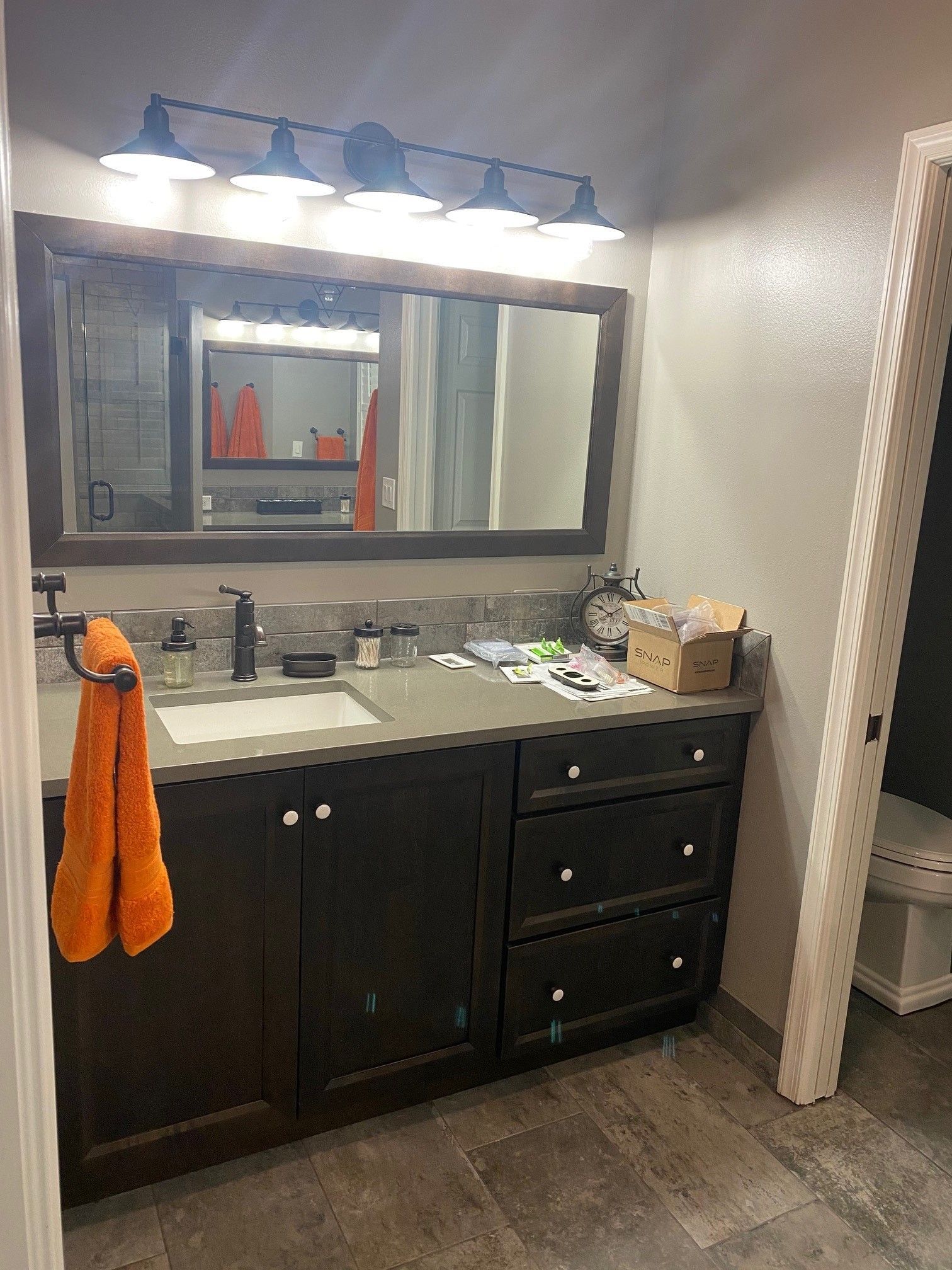 Bathroom vanity with dark cabinets, a mirror, and an orange towel.