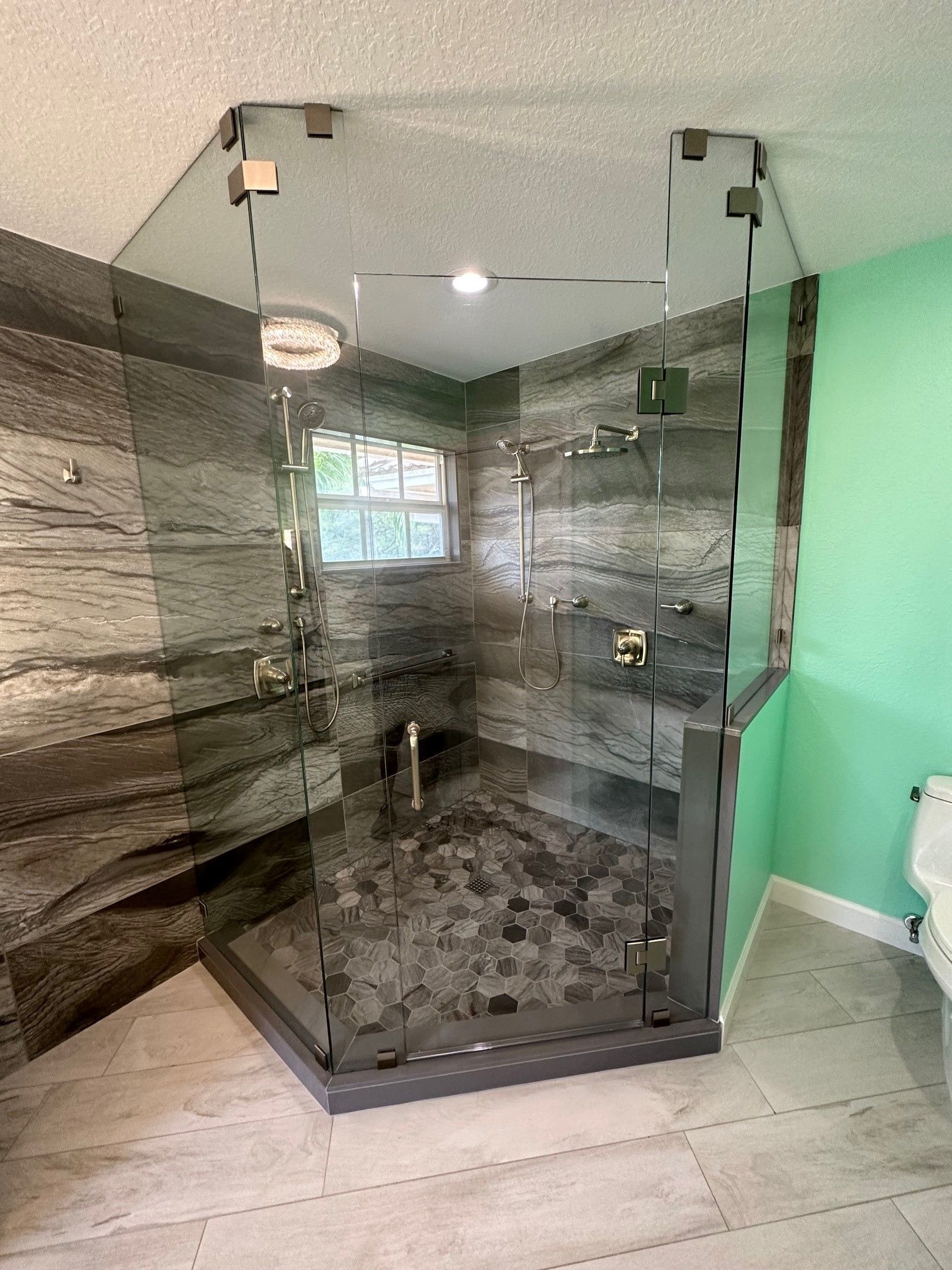 Modern glass shower with gray stone tile walls and flooring; green wall.