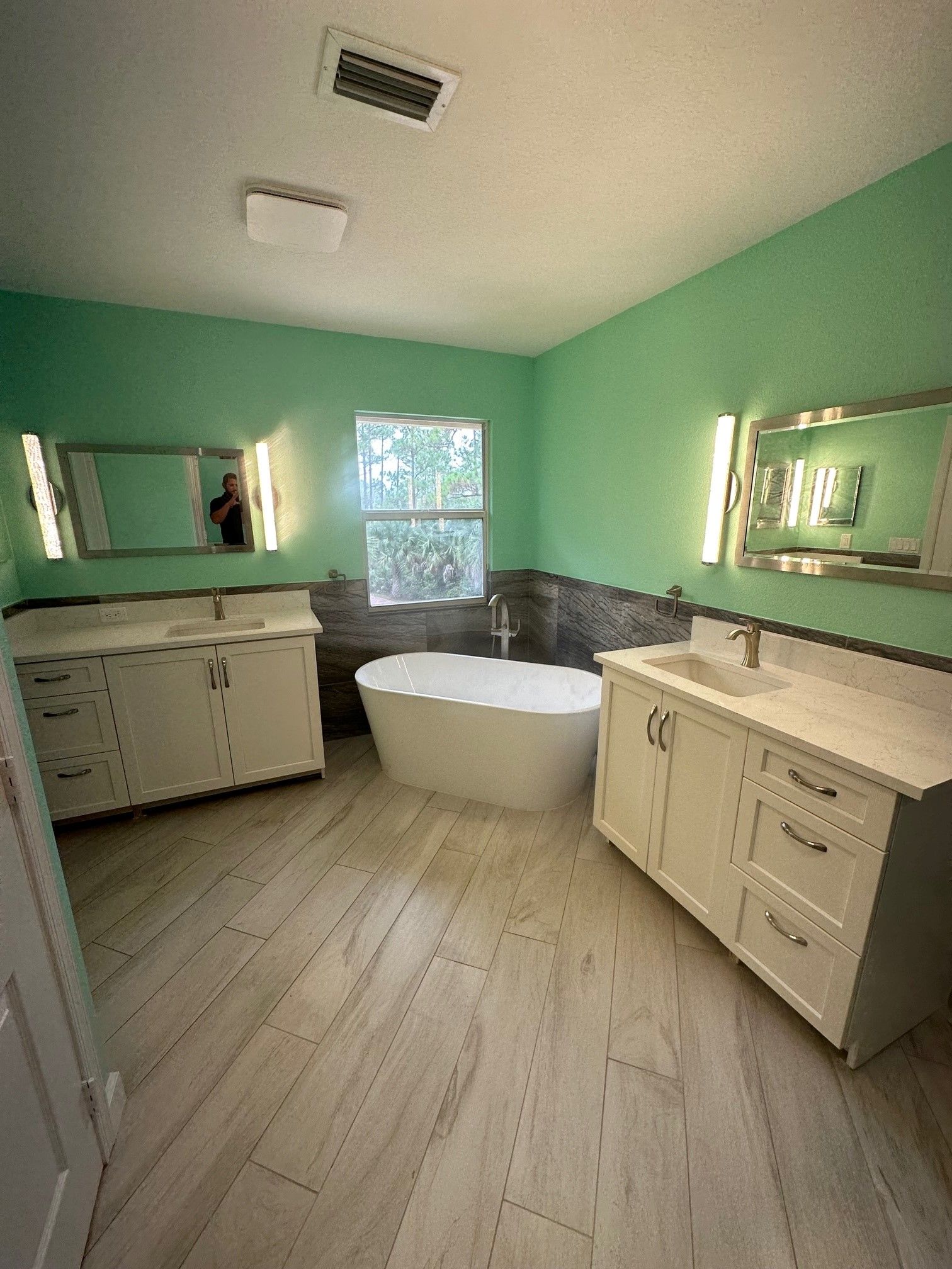 Spacious bathroom with green walls, two vanities, a freestanding tub, and light wood-look flooring.
