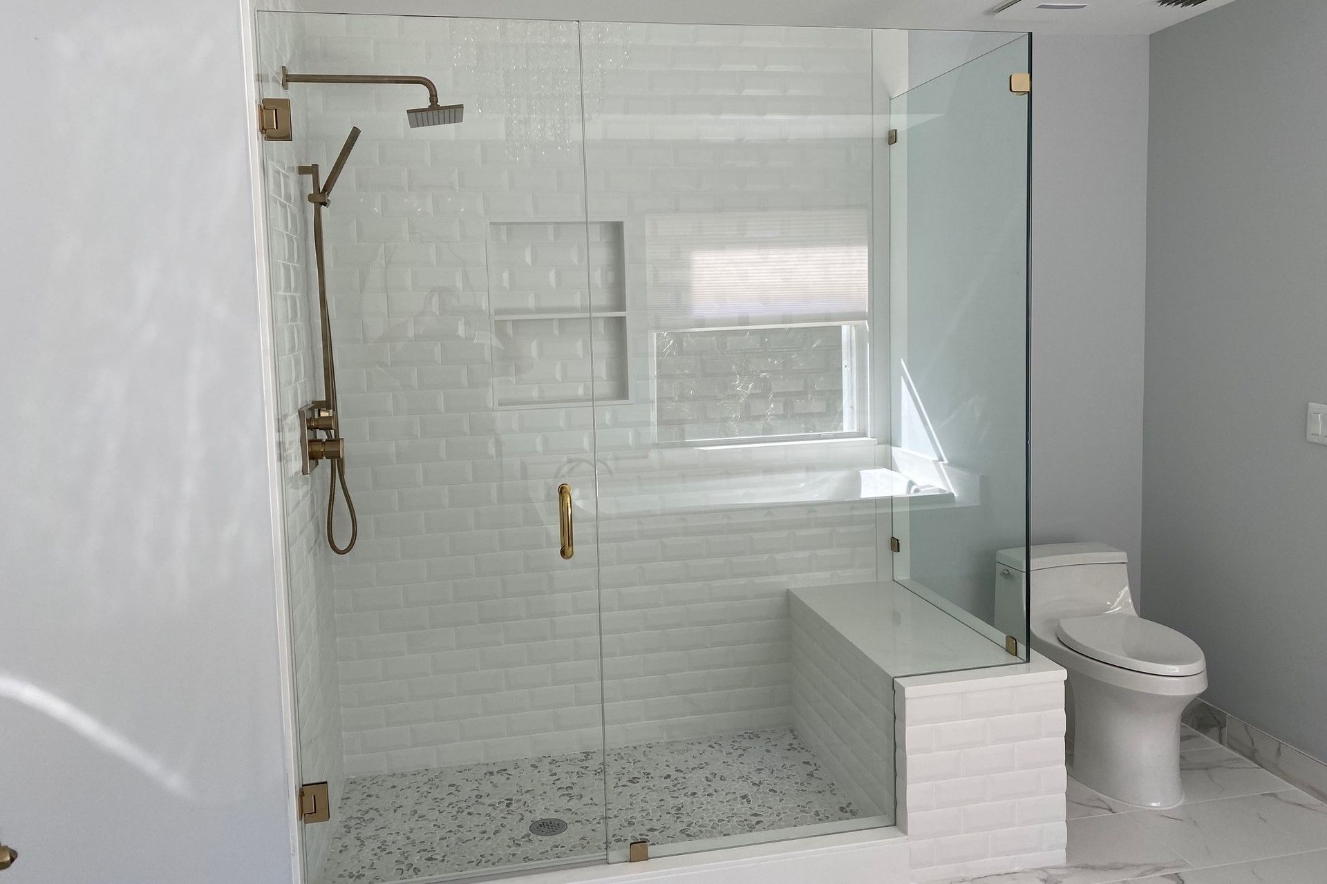 Modern bathroom with glass shower, subway tile, bench, and a toilet.