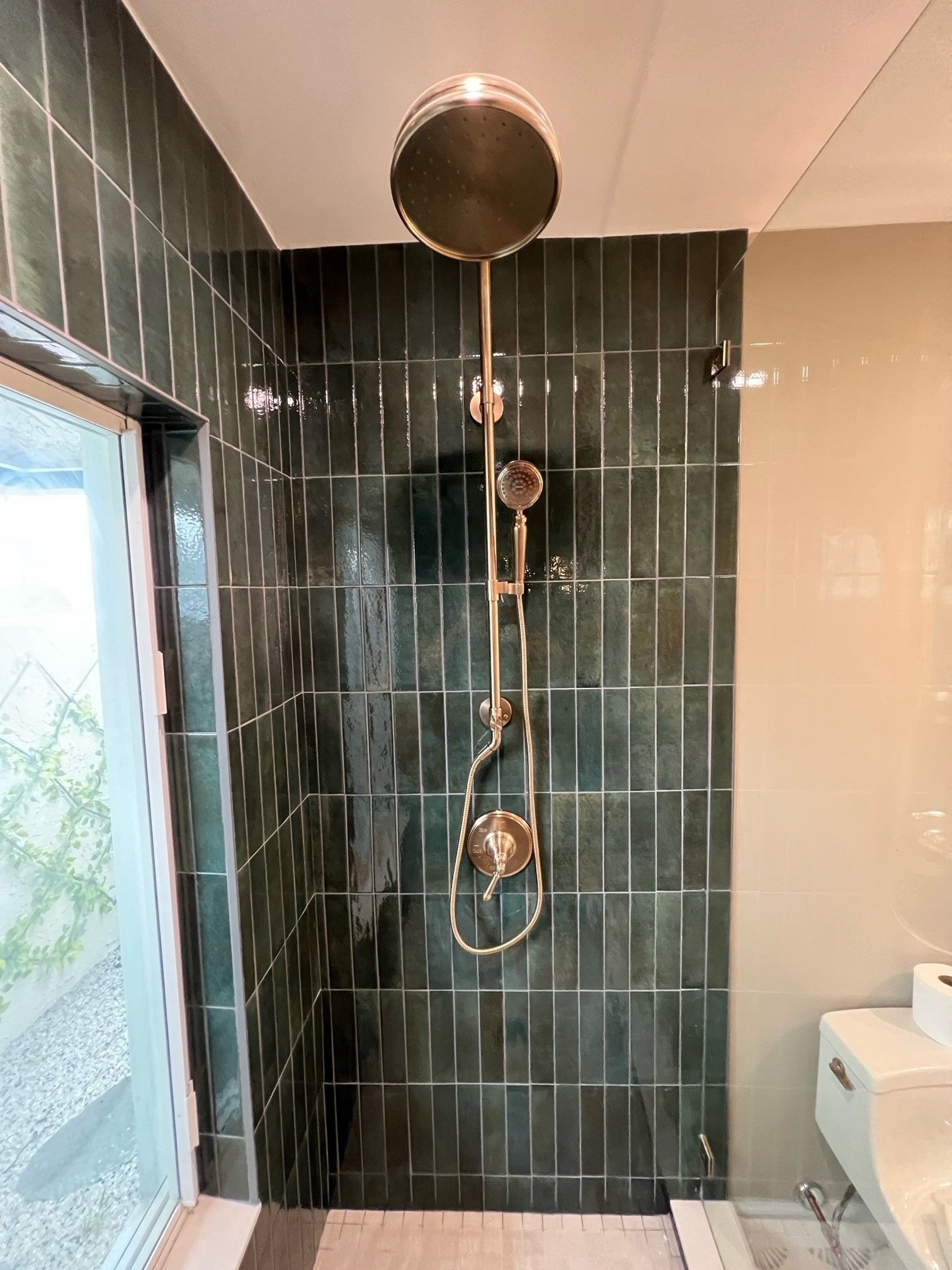 Dark green tiled shower with brass fixtures, including a rain shower head and handheld sprayer.