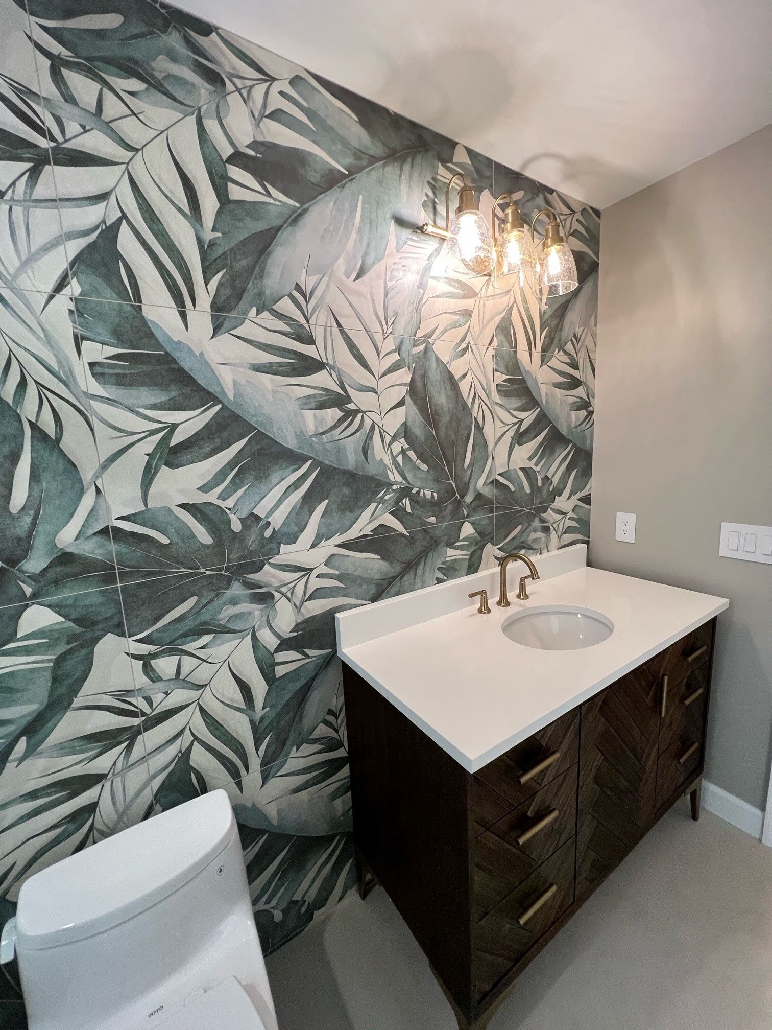 Powder room with tropical leaf wallpaper, dark wood vanity, white countertop, and white toilet.