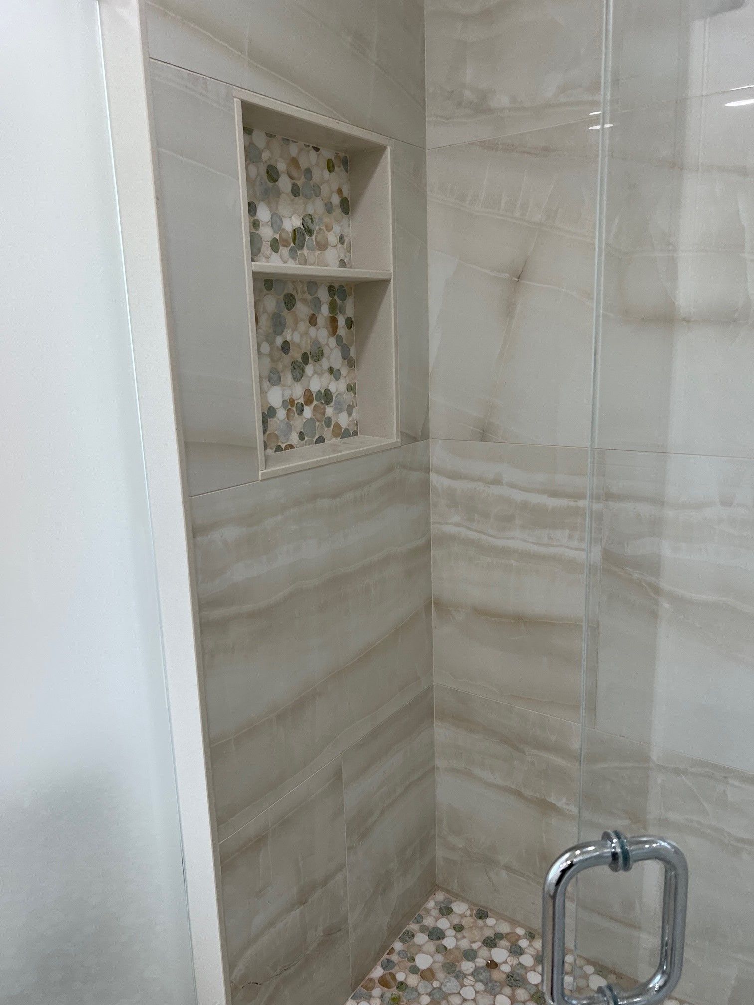 Shower with tiled walls, built-in shelving, and a pebble tile floor.