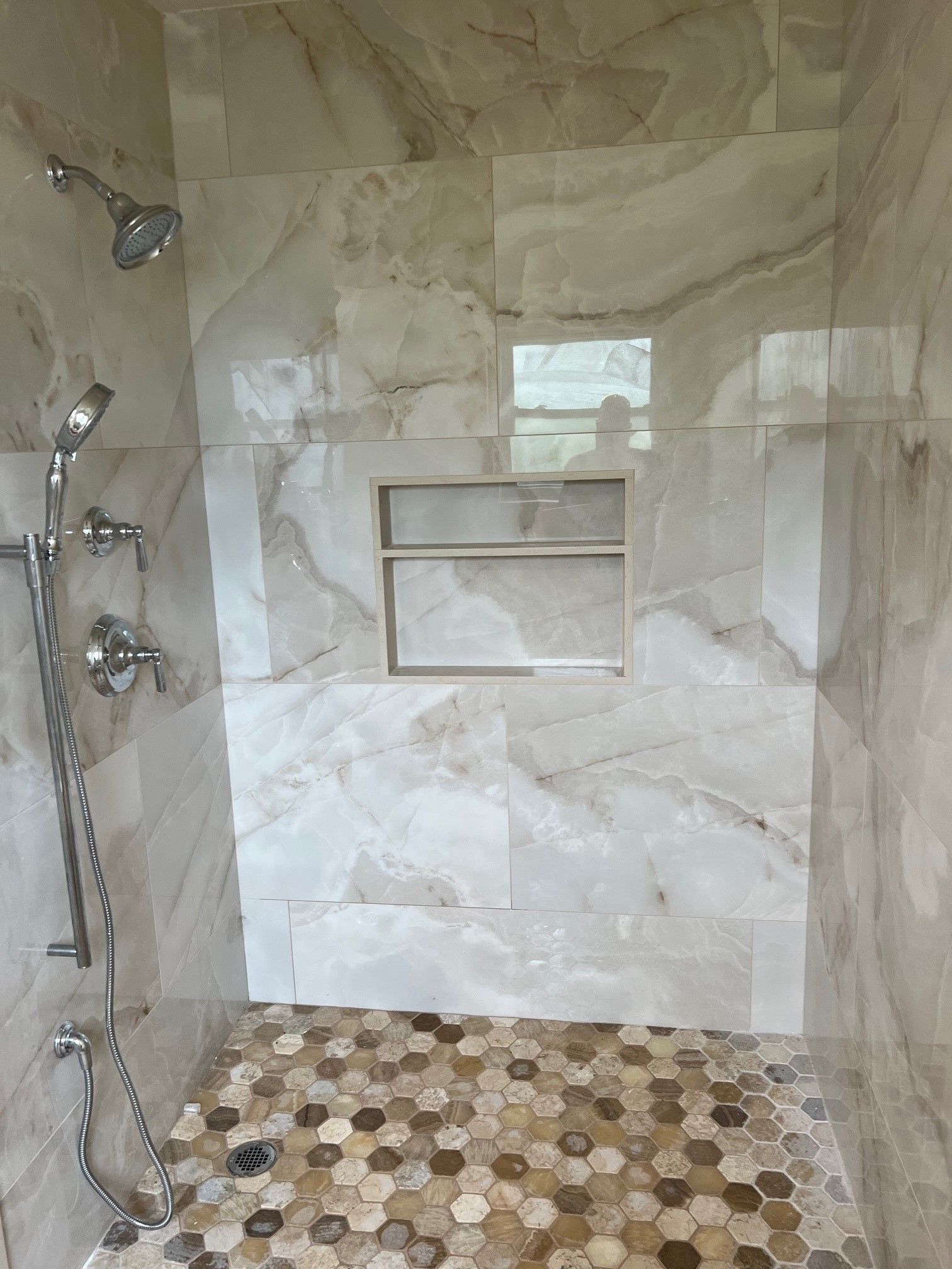 Shower with beige marbled tile walls, a mosaic tile floor, and a built-in shelf.
