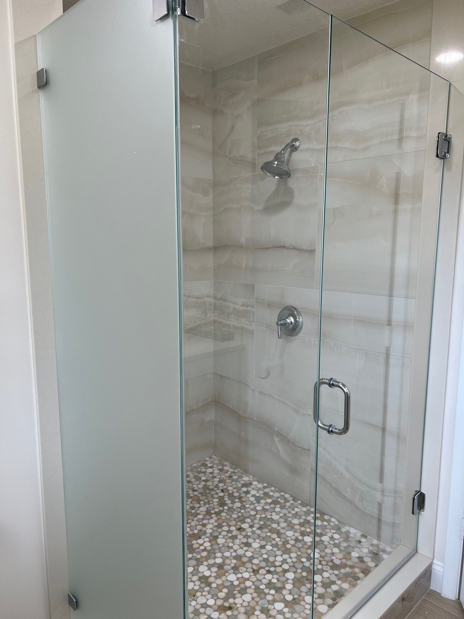 A modern glass shower enclosure with frosted glass panel and pebble floor.