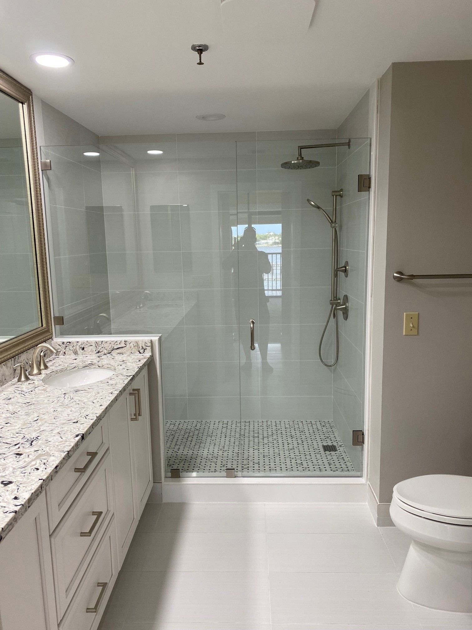 Bathroom with white walls, shower with glass doors, white vanity, and toilet.