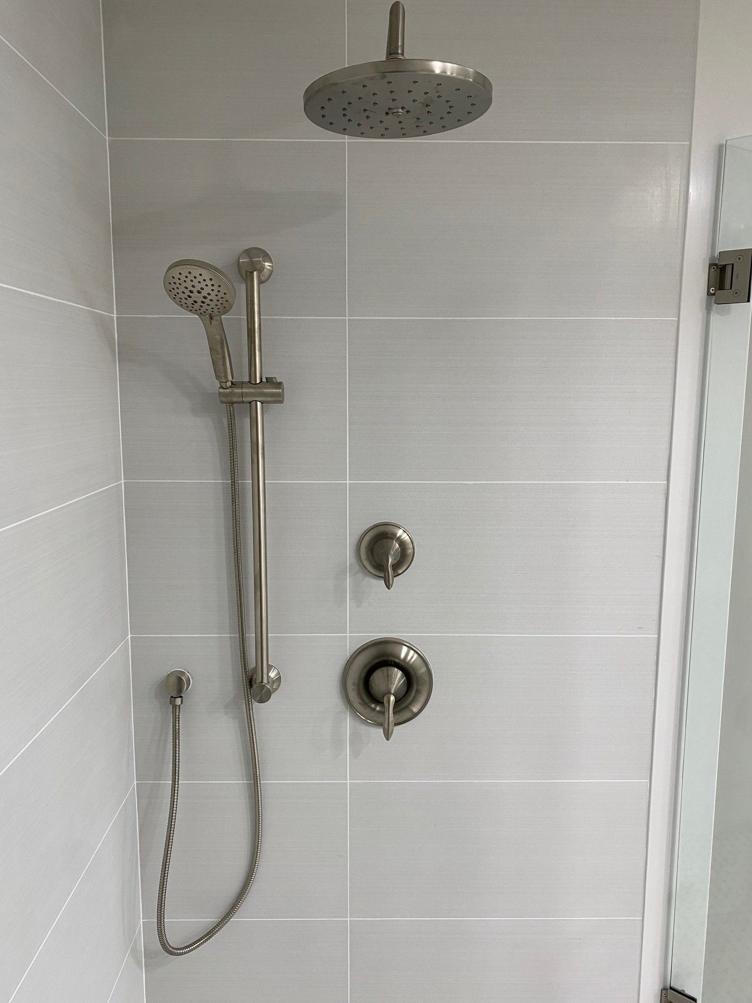 Gray tiled shower with a silver rain showerhead, handheld shower, and control knobs.