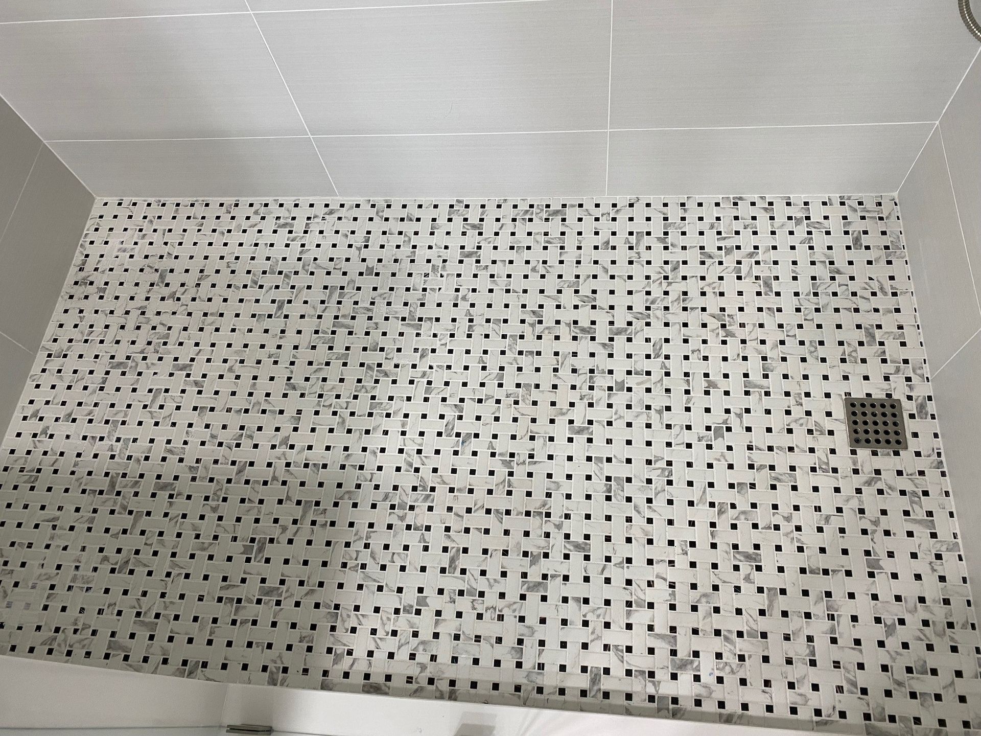 Shower floor with small, white and gray mosaic tiles; a drain is visible.