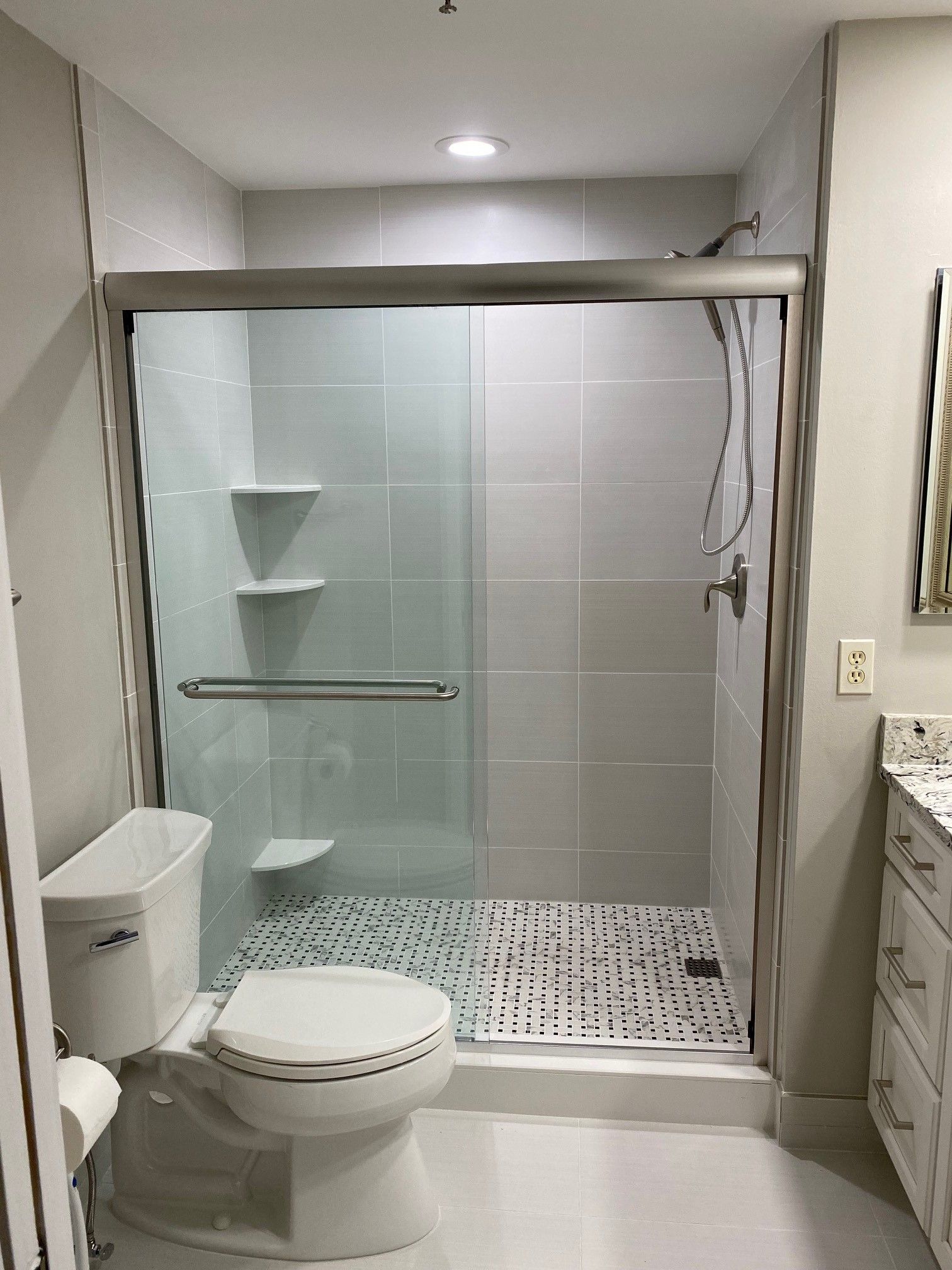 Bathroom with a glass shower, toilet, and vanity. Gray tile and white fixtures.