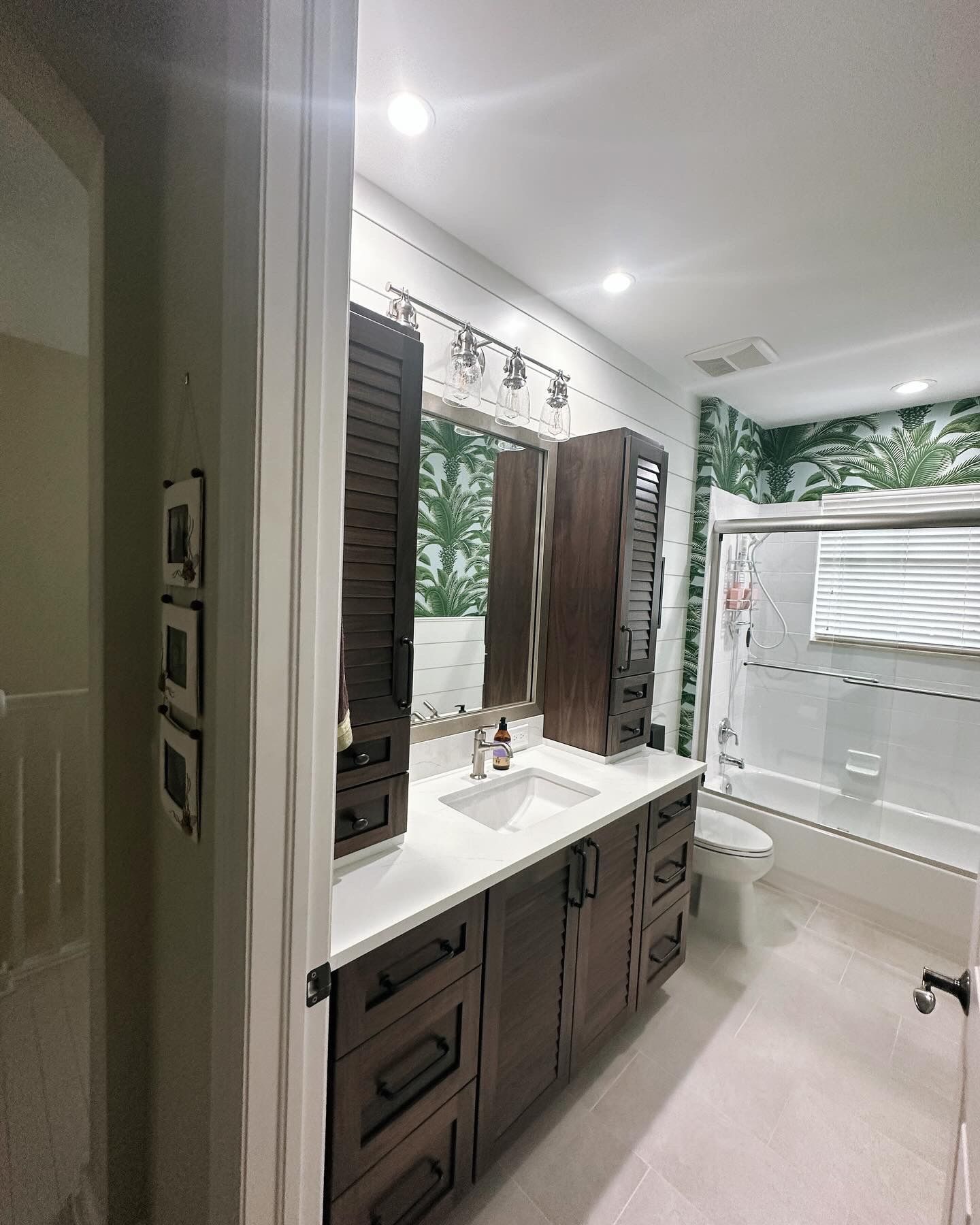 Bathroom with a white countertop, dark wood cabinets, and tropical wallpaper.