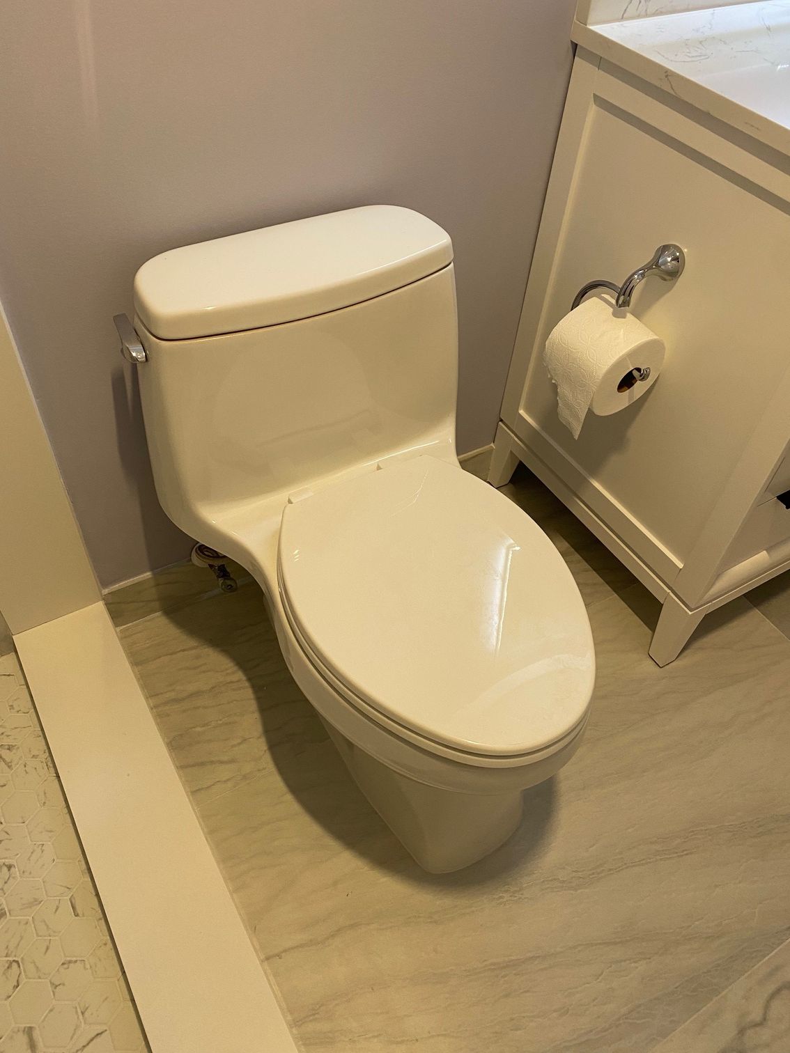White toilet in a bathroom, near a cabinet with toilet paper.