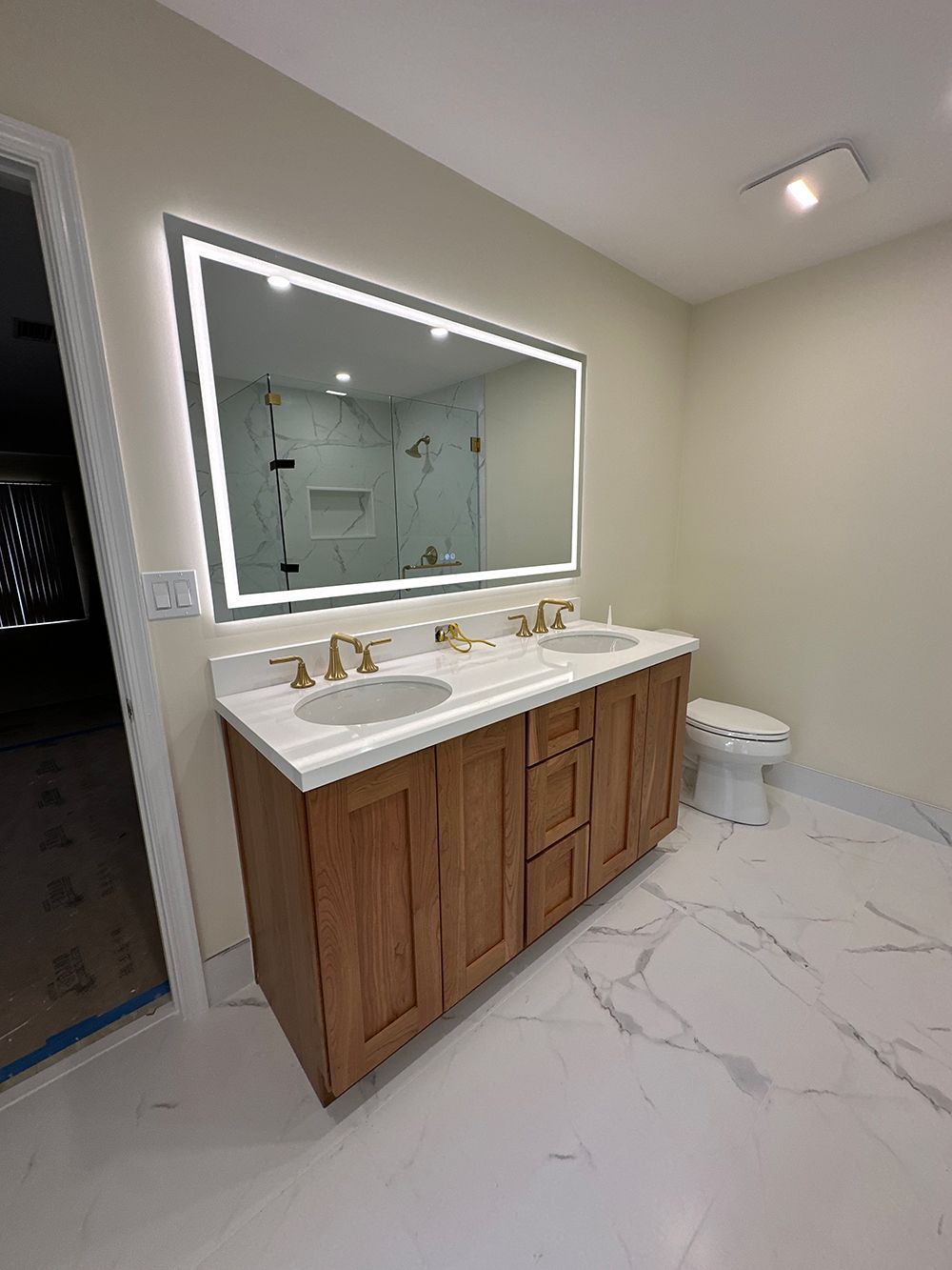 Bathroom with a wooden vanity, double sinks, and a large mirror with LED lighting.